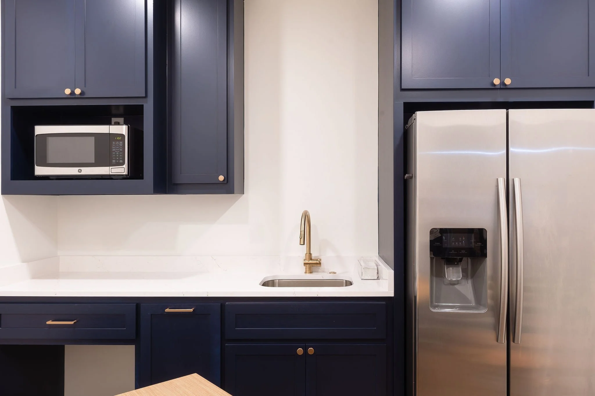 Kitchen with navy blue cabinets, a white countertop, stainless steel refrigerator with water and ice dispenser, and a microwave oven.