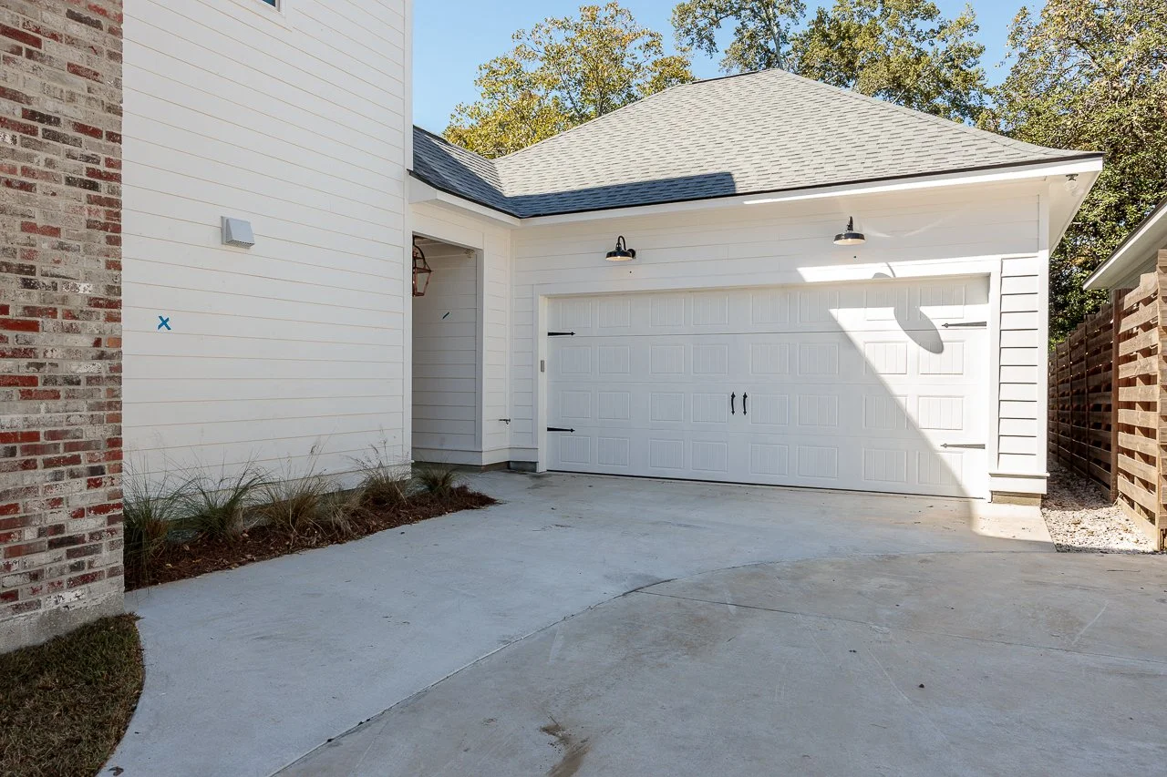 White garage door with a driveway and side entrance, brick wall on the left, wooden fence on the right.