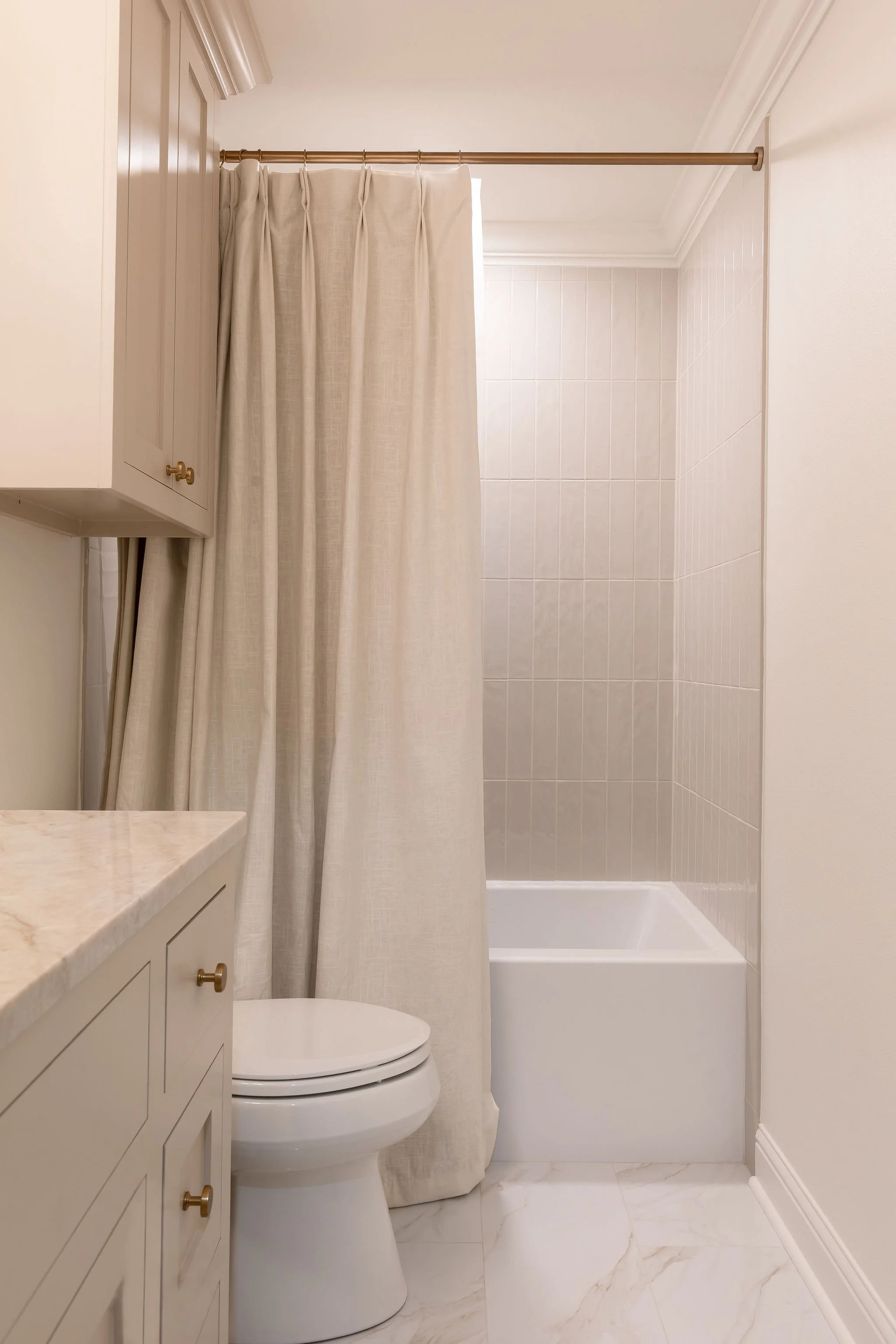 Bathroom with a shower and curtain, toilet, and beige cabinetry.