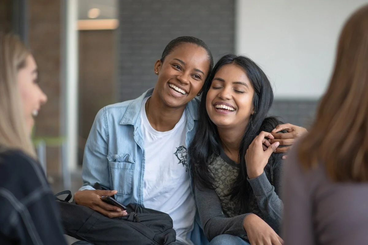 A photo of two young women sitting side by side with their arms around eachother