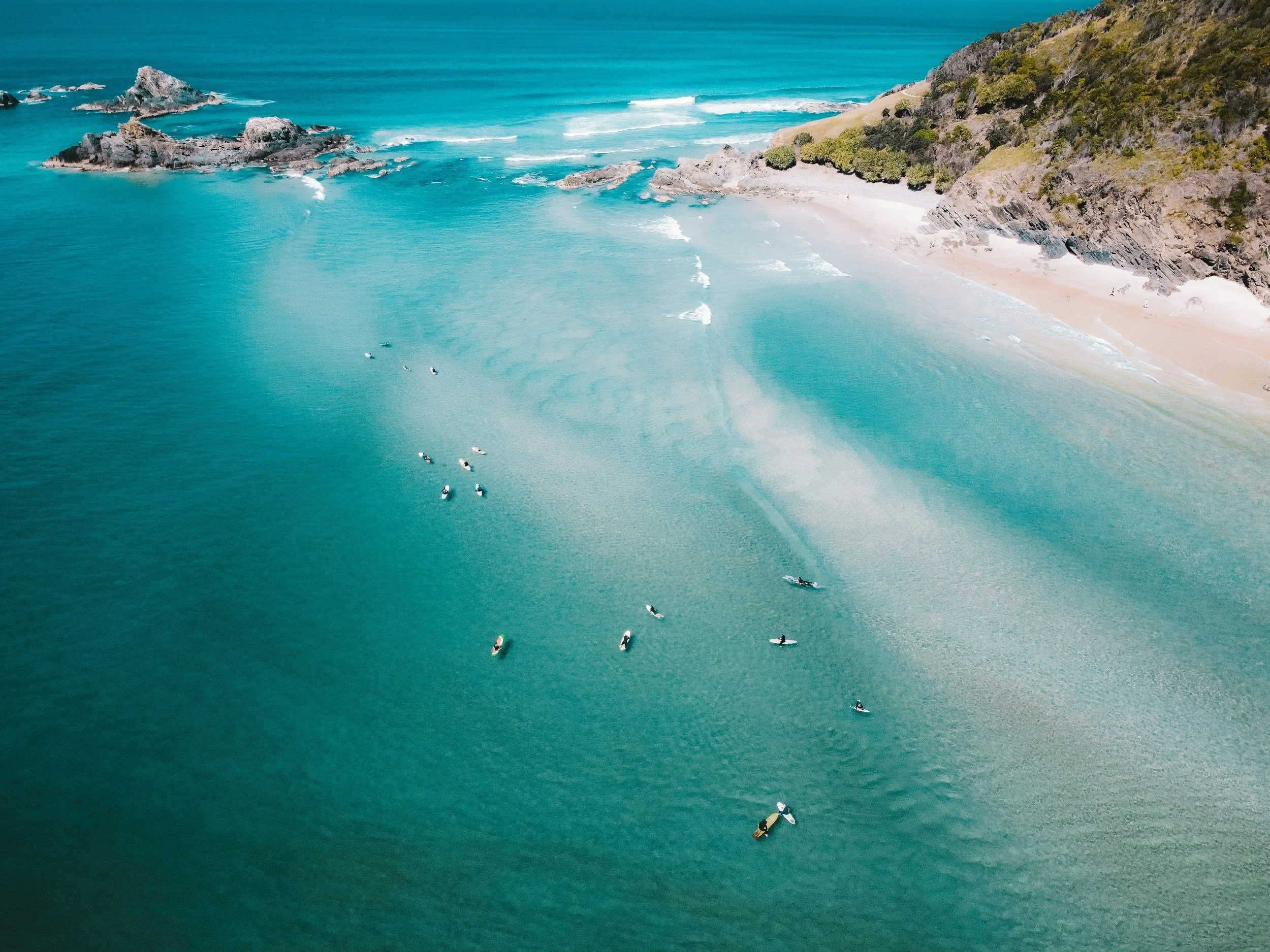 Blackmore's Pressure and Window Cleaning services Northern Rivers, NSW, Australia. Aerial view of a beach with turquoise water, sandy shore, rocky outcroppings, and lush green hillside, with several small boats on the water.