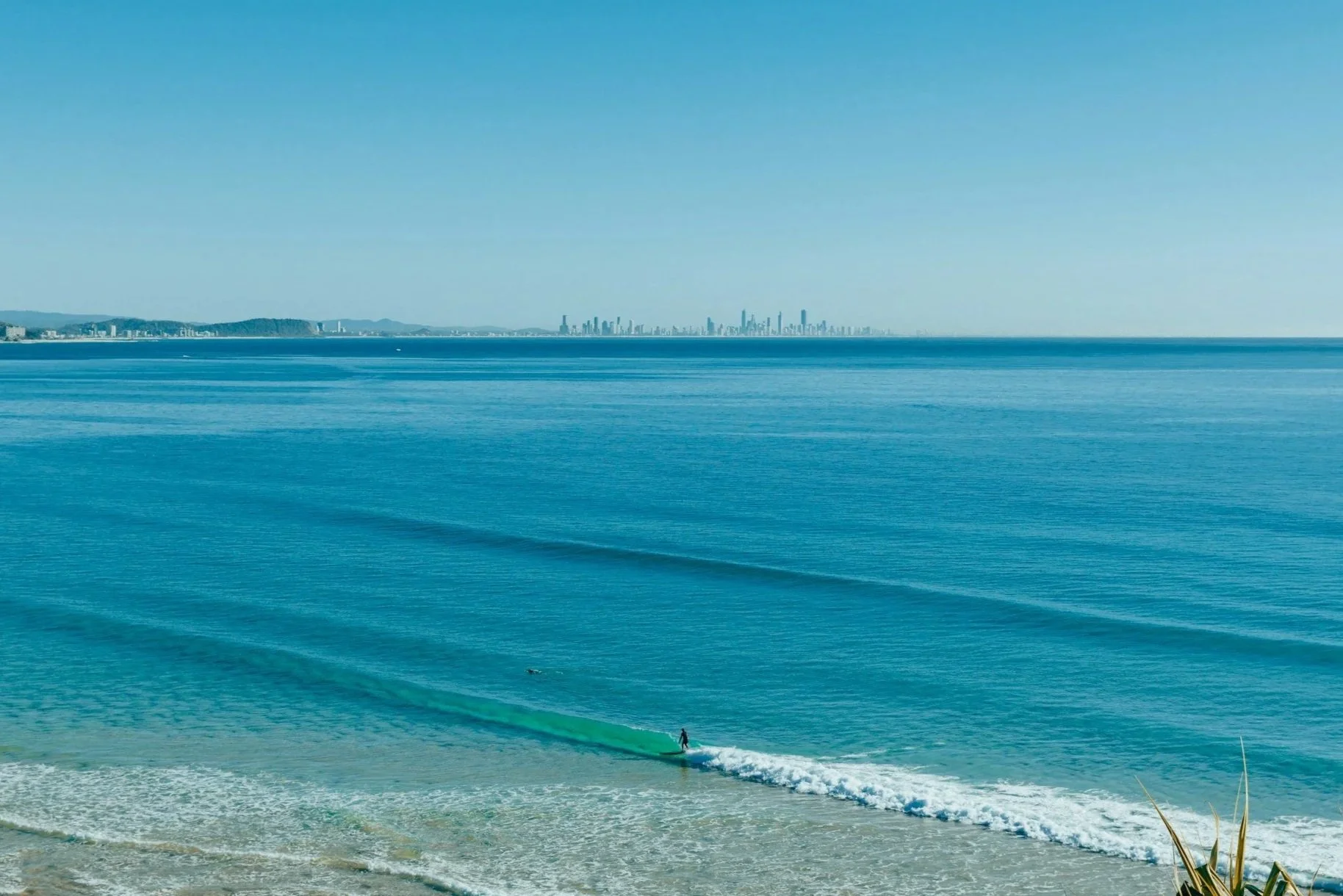 Blackmore's Pressure and Window Cleaning services the Gold Coast, Queensland, Australia. Person surfing on the ocean waves near the beach and the distant city skyline in the background.