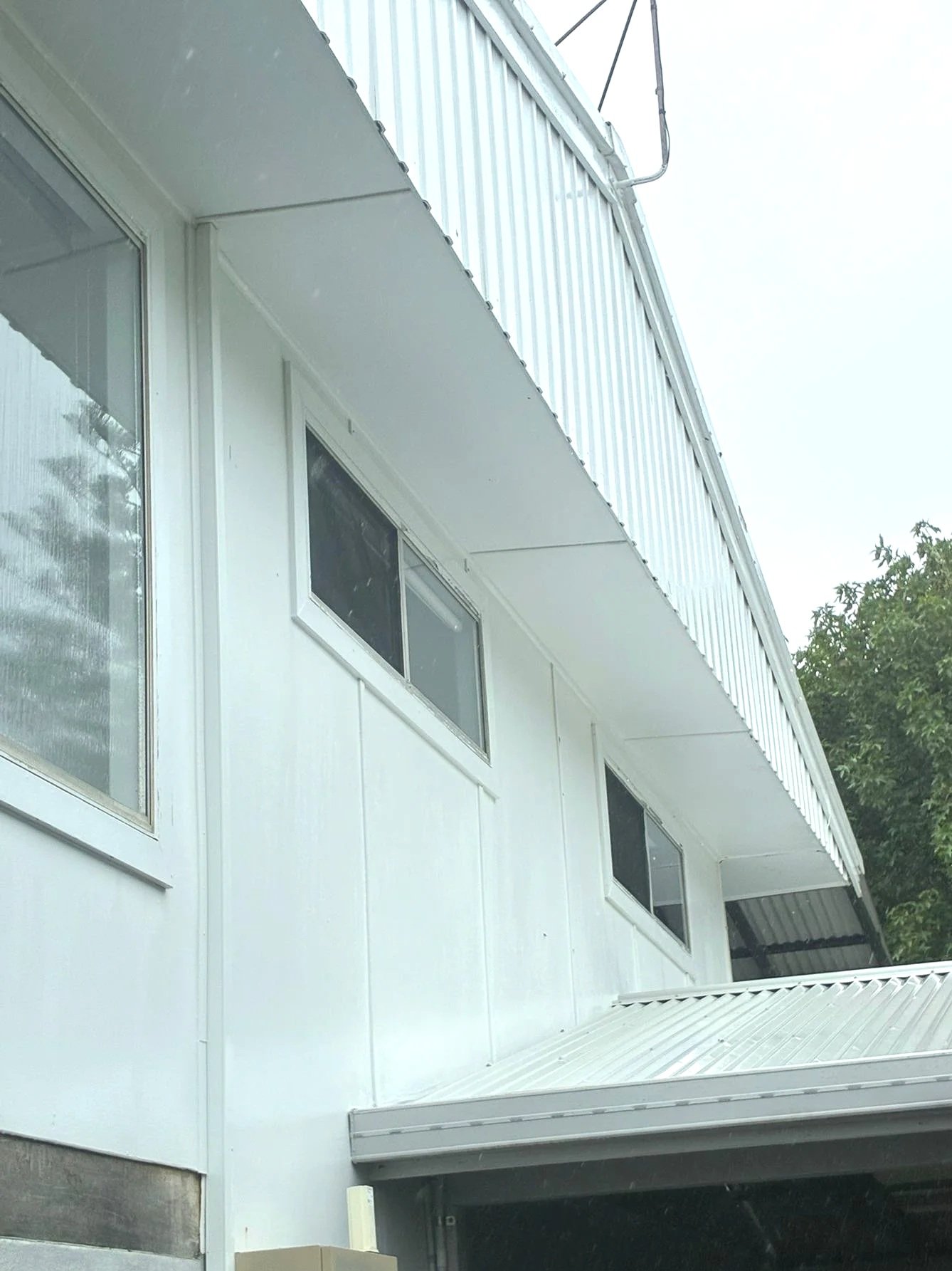 Exterior view of a white building with three rectangular windows and a metal awning, viewed from below.