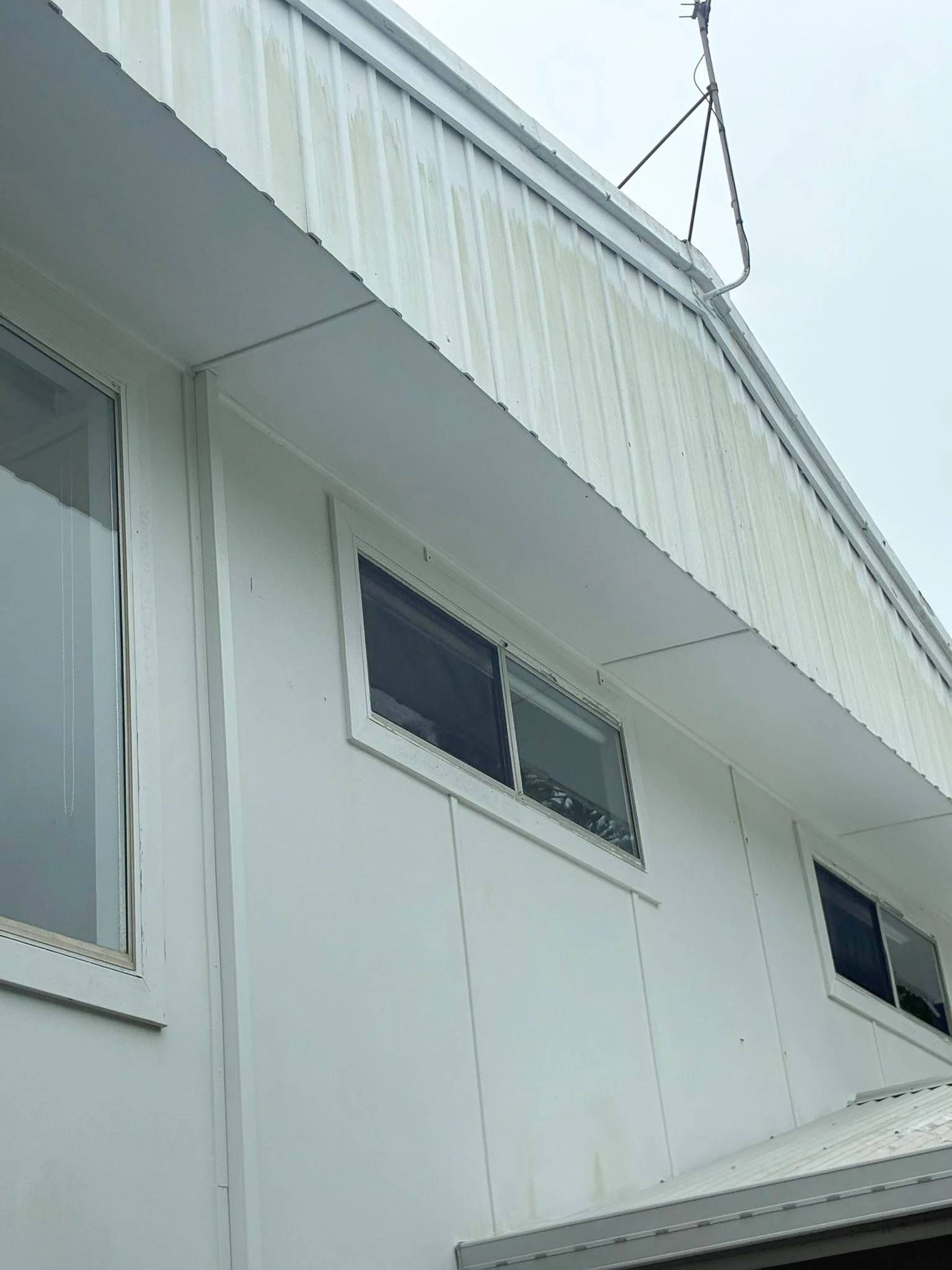 Close-up of a white house's exterior with three windows and an antenna on the roof.
