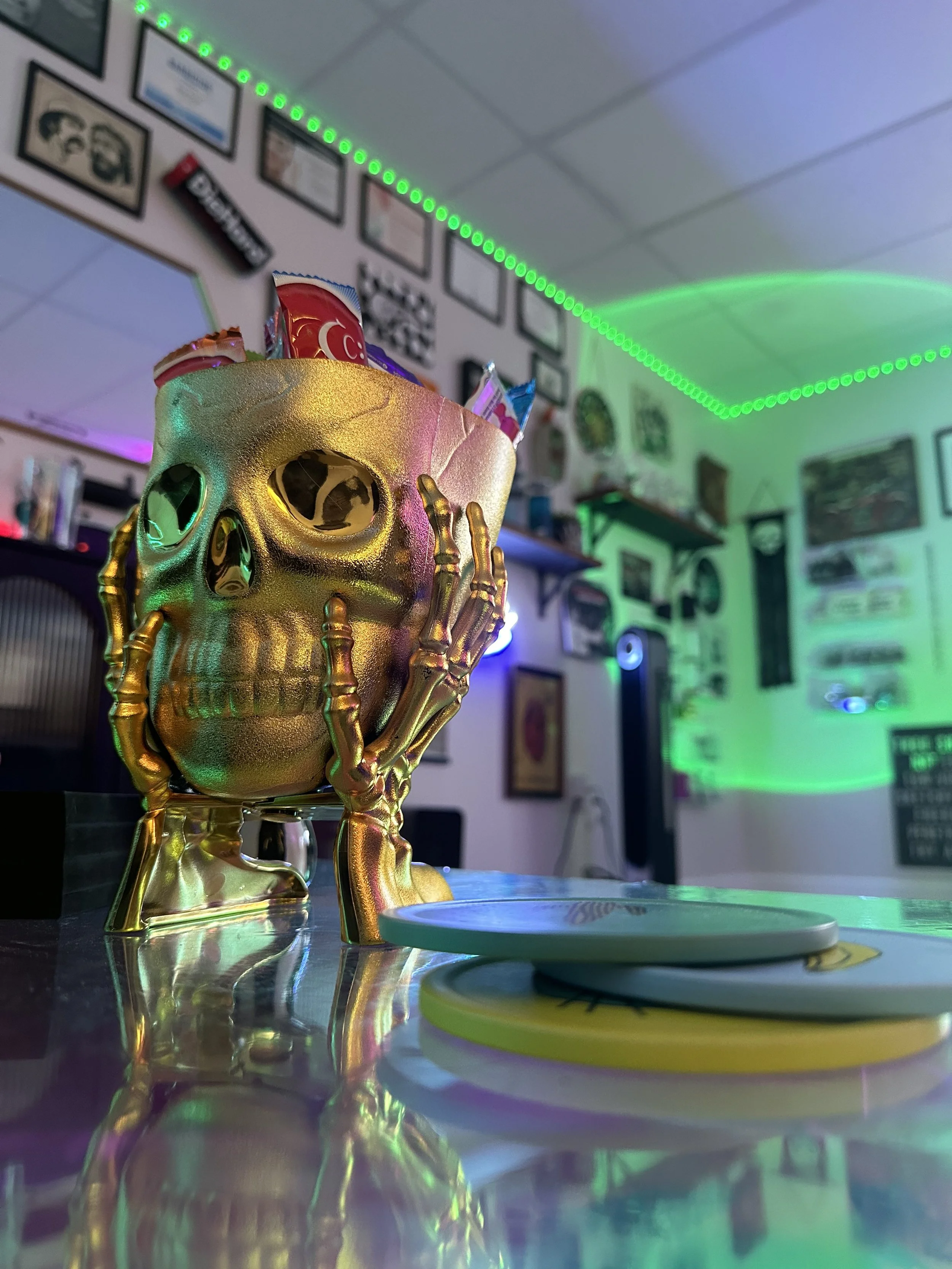 gold skull-shaped candy dish on reflective surface. neon green and purple light