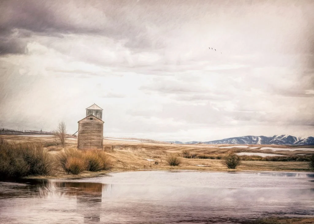 ISOLATED GRAIN ELEVATOR REFLECTED IN A QUIET POND WITH SNOWY MOUNTAINS IN THE DISTANCE