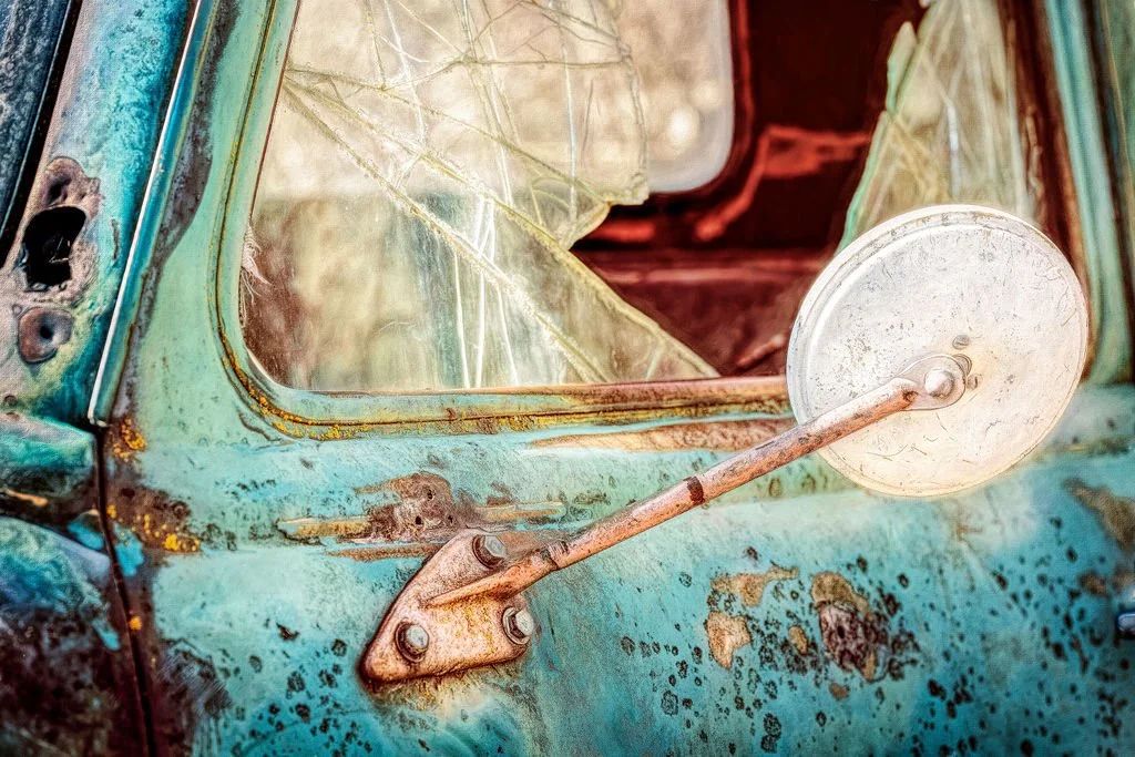 CLOSE-UP OF A BROKEN WINDOW AND RUSTED MIRROR ON A WEATHERED TEAL TRUCK DOOR - 1949 GMC PICKUP TRUCK