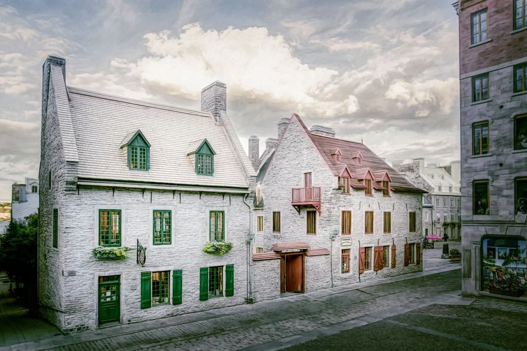 Painterly photograph of historic whitewashed stone buildings along a quiet cobblestone street in Old Quebec City under dramatic clouds and soft light.