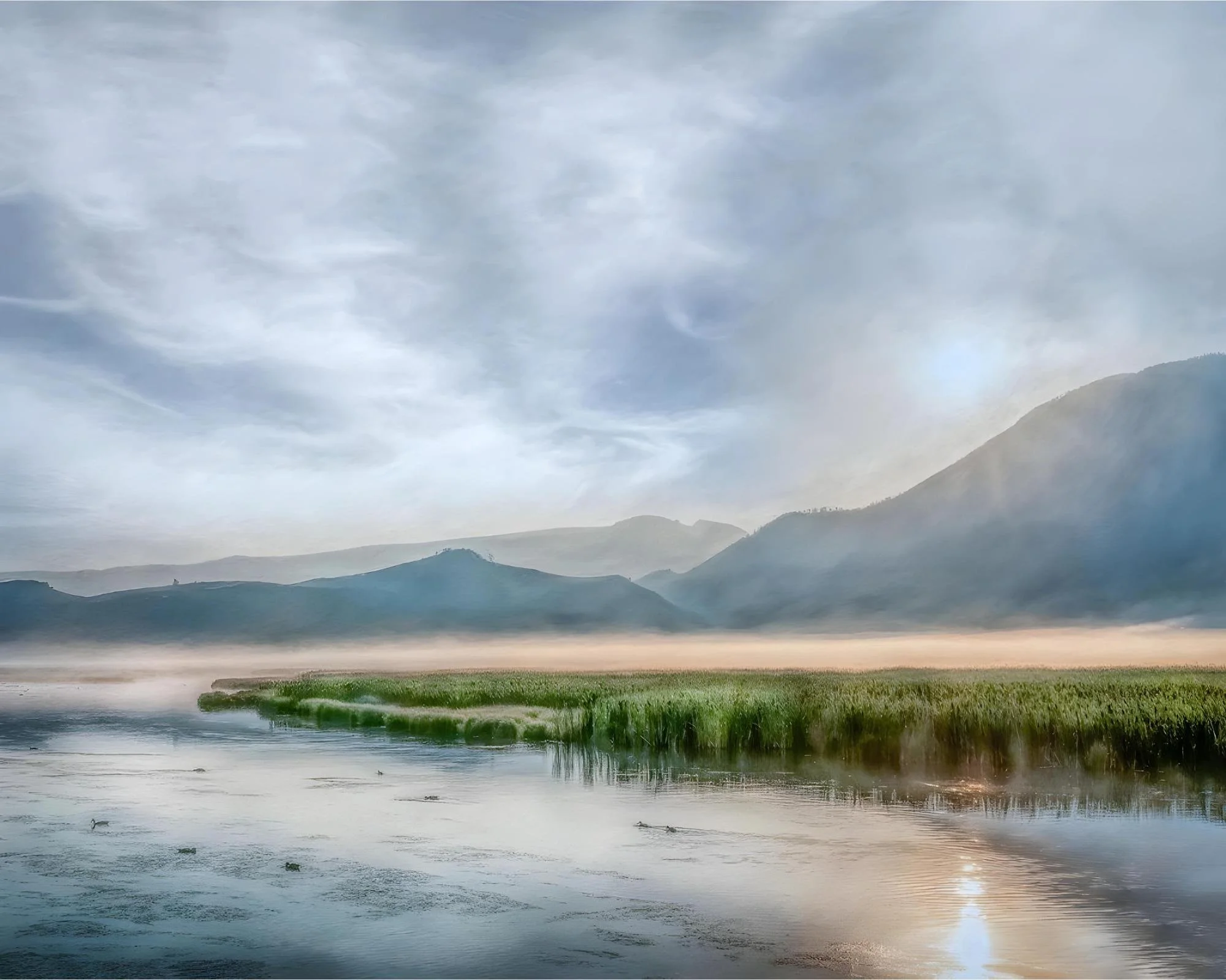 SERENE MISTY WETLAND LANDSCAPE WITH STILL WATER, GREEN REEDS, AND SOFTLY LAYERED MOUNTAINS UNDER A PALE MORNING SKY