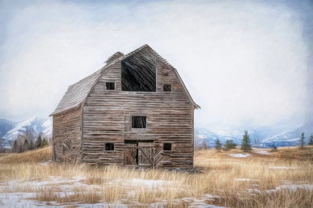 RUSTIC BARN WALL ART OF A WEATHERED WOODEN BARN IN A WINTER FIELD WITH DISTANT MOUNTAINS UNDER A SOFT, PALE SKY