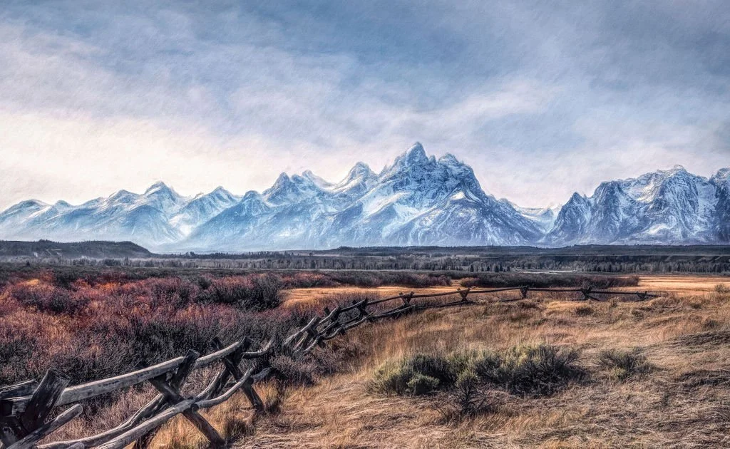 Snow-capped Teton Mountain Range in the background with a wooden fence crossing a grassy field in the foreground.