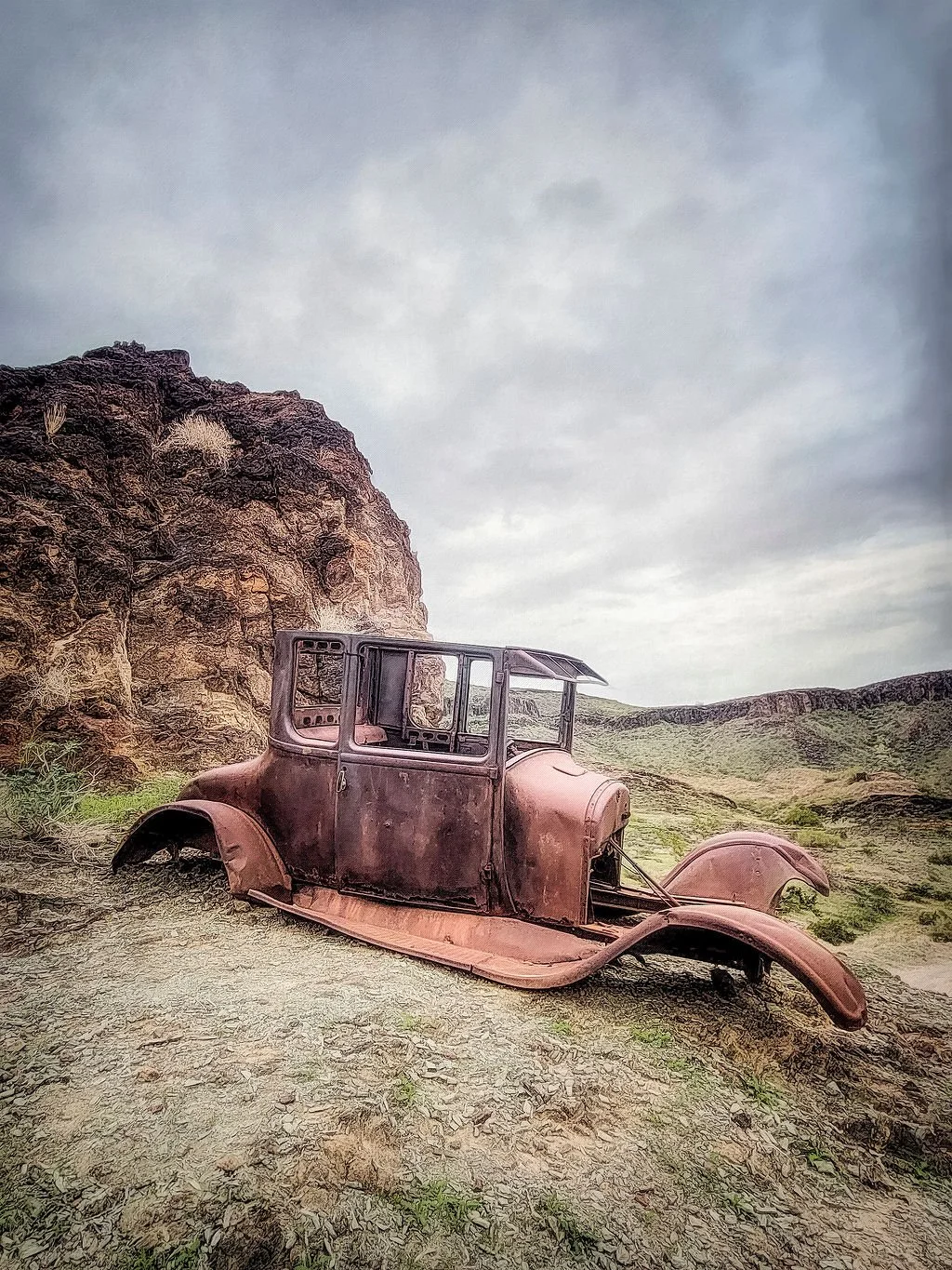RUSTED ABANDONED CAR IN A DESERT LANDSCAPE BELOW WEATHERED ROCK FORMATIONS AT THE DESERT BAR, PARKER, ARIZONA