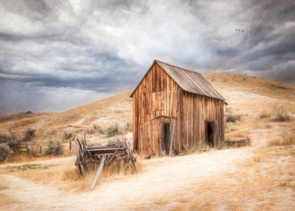 
WEATHERED WOODEN BARN IN A DRY HILLSIDE LANDSCAPE UNDER A STORMY SKY BANNACK CITY, MONTANA 