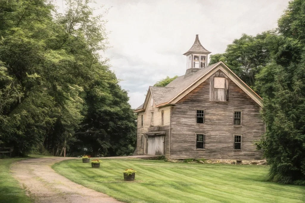 an historic weathered barn near Boothbay Harbor, Maine surrounded by trees and a green lawn.