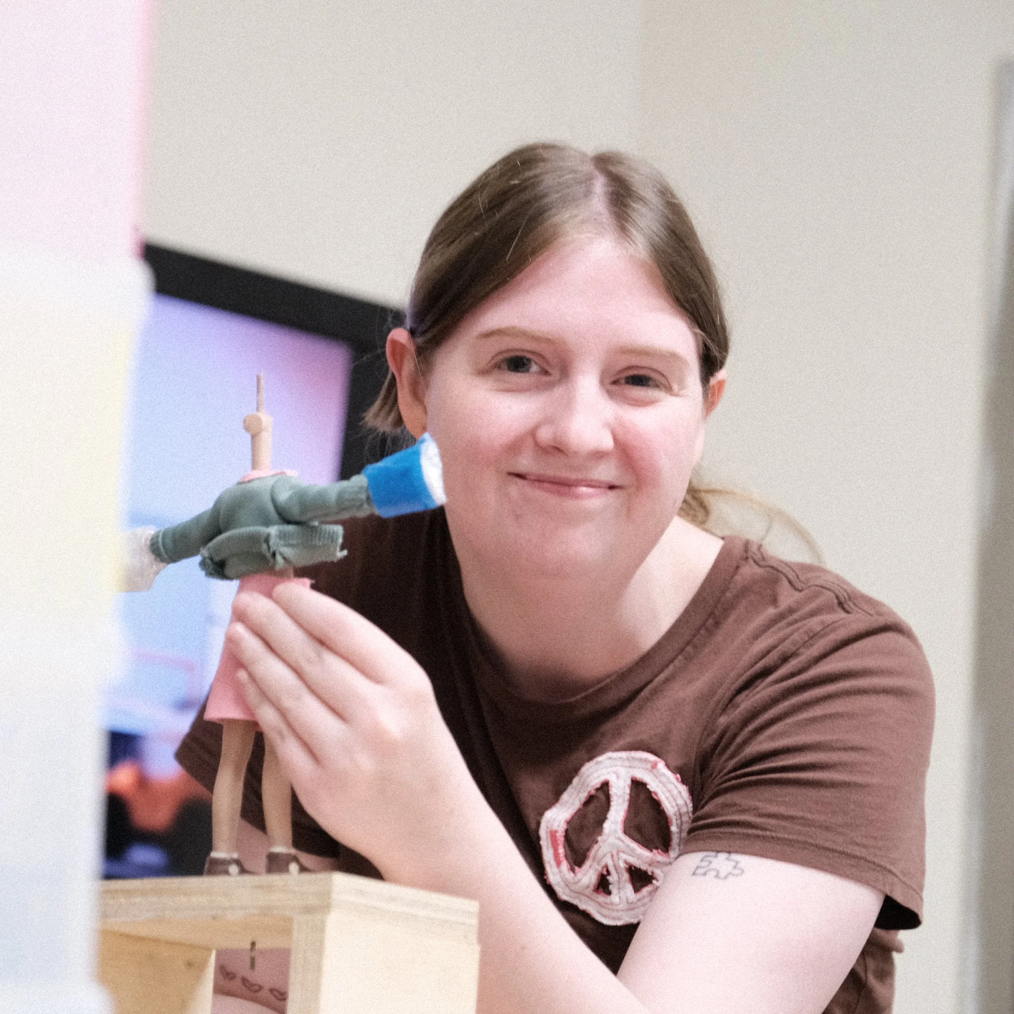 A woman smiling and holding a small robotic figure, with a computer monitor in the background.