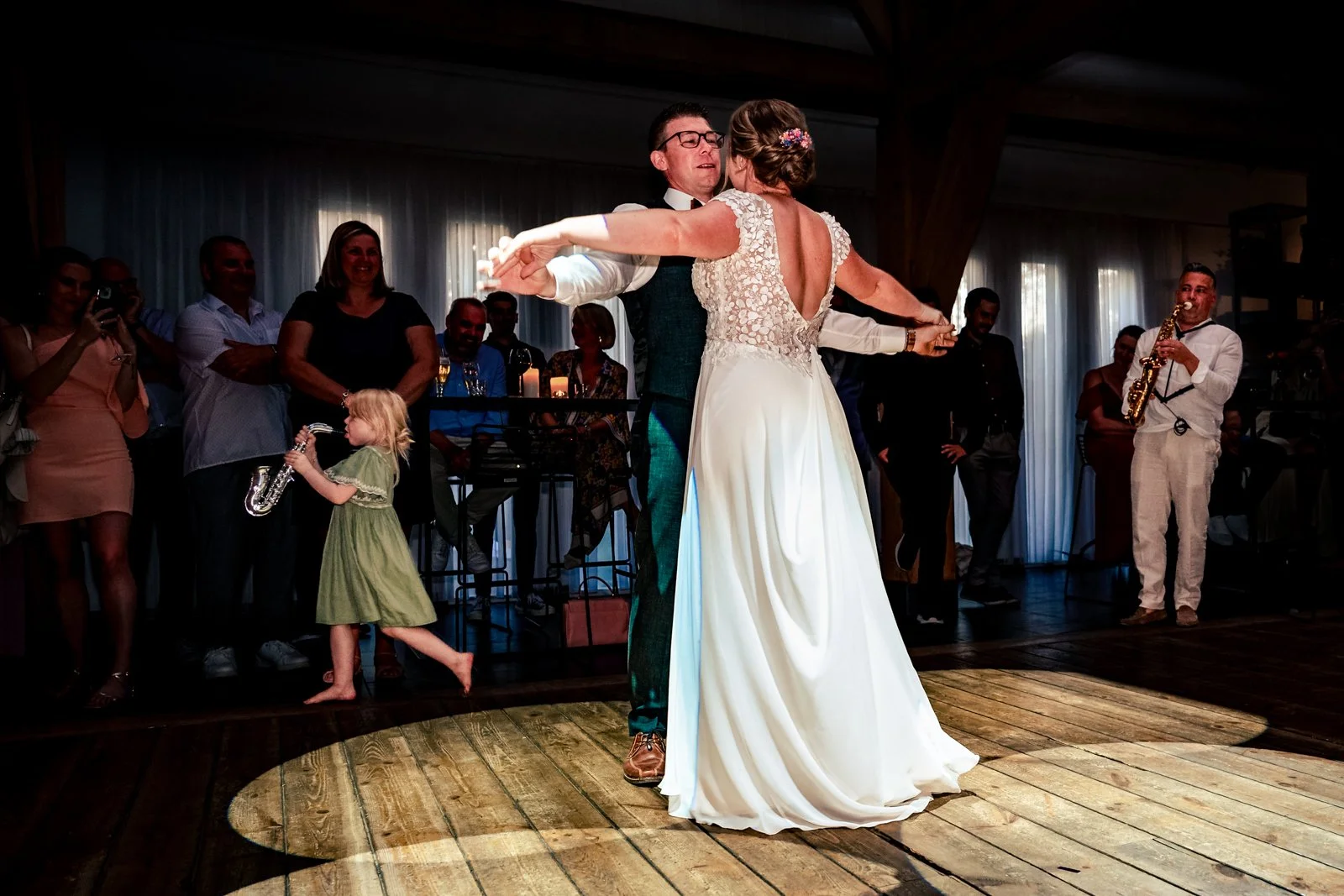 Bruid en bruidegom dansen op de dansvloer tijdens hun bruiloft, terwijl gasten kijken en op de achtergrond live muziek wordt gespeeld.