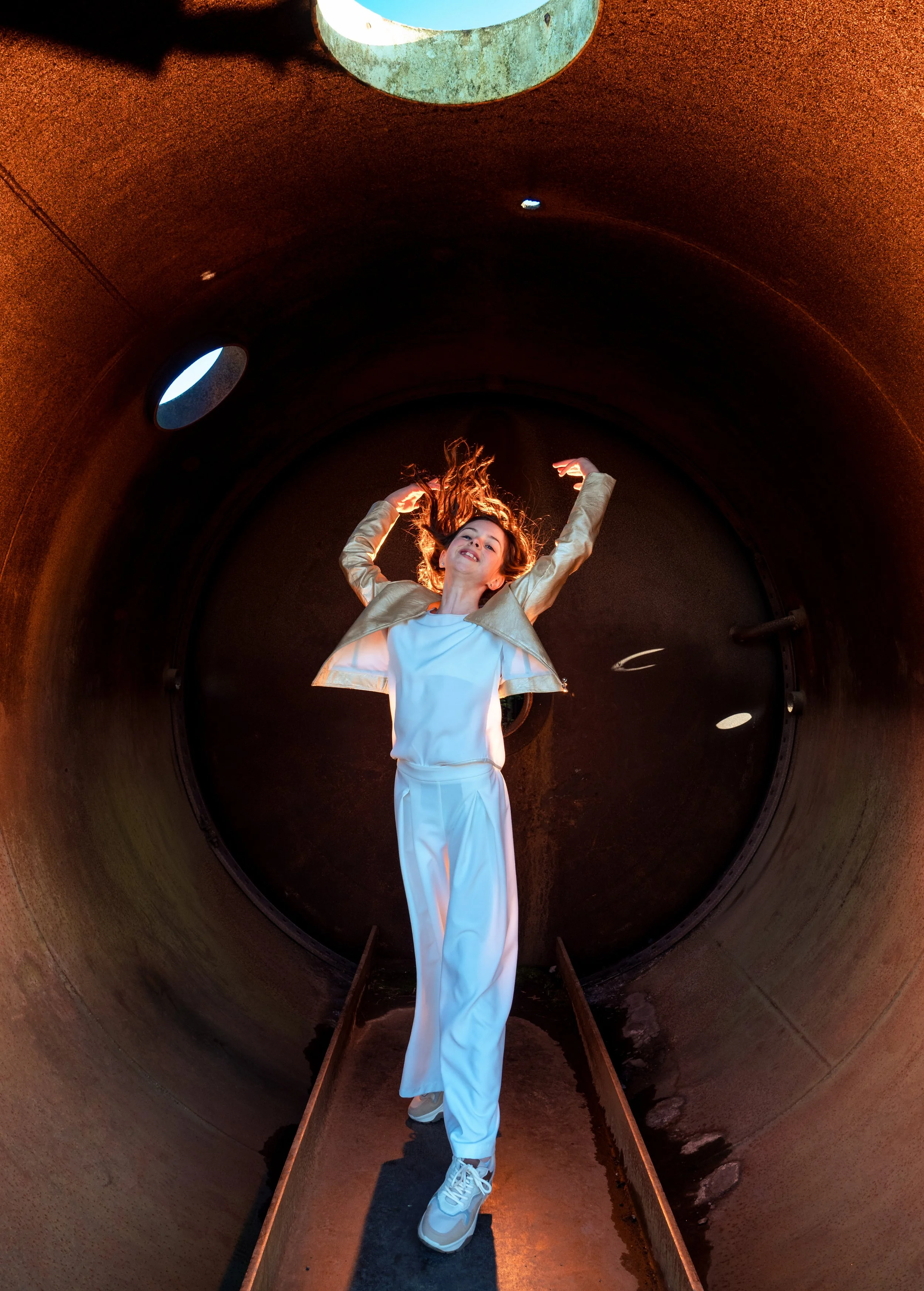 Vrouw danst in een grote, ronde, metalen buisruimte met kleine ronde vensters en dim verlichte omgeving.