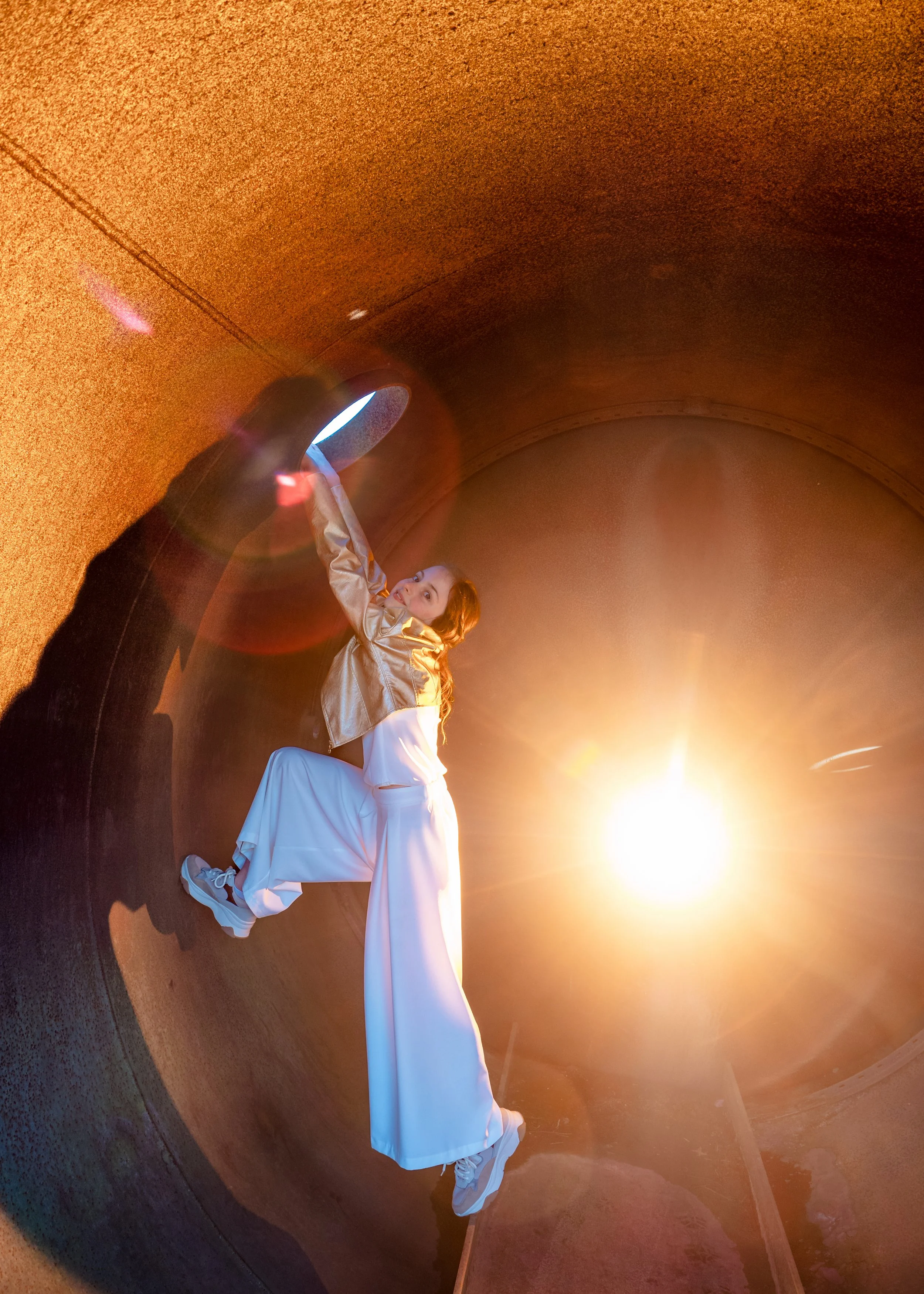 Een vrouw die zich op de muur van een tunnel hangt, met een zonsondergang op de achtergrond.