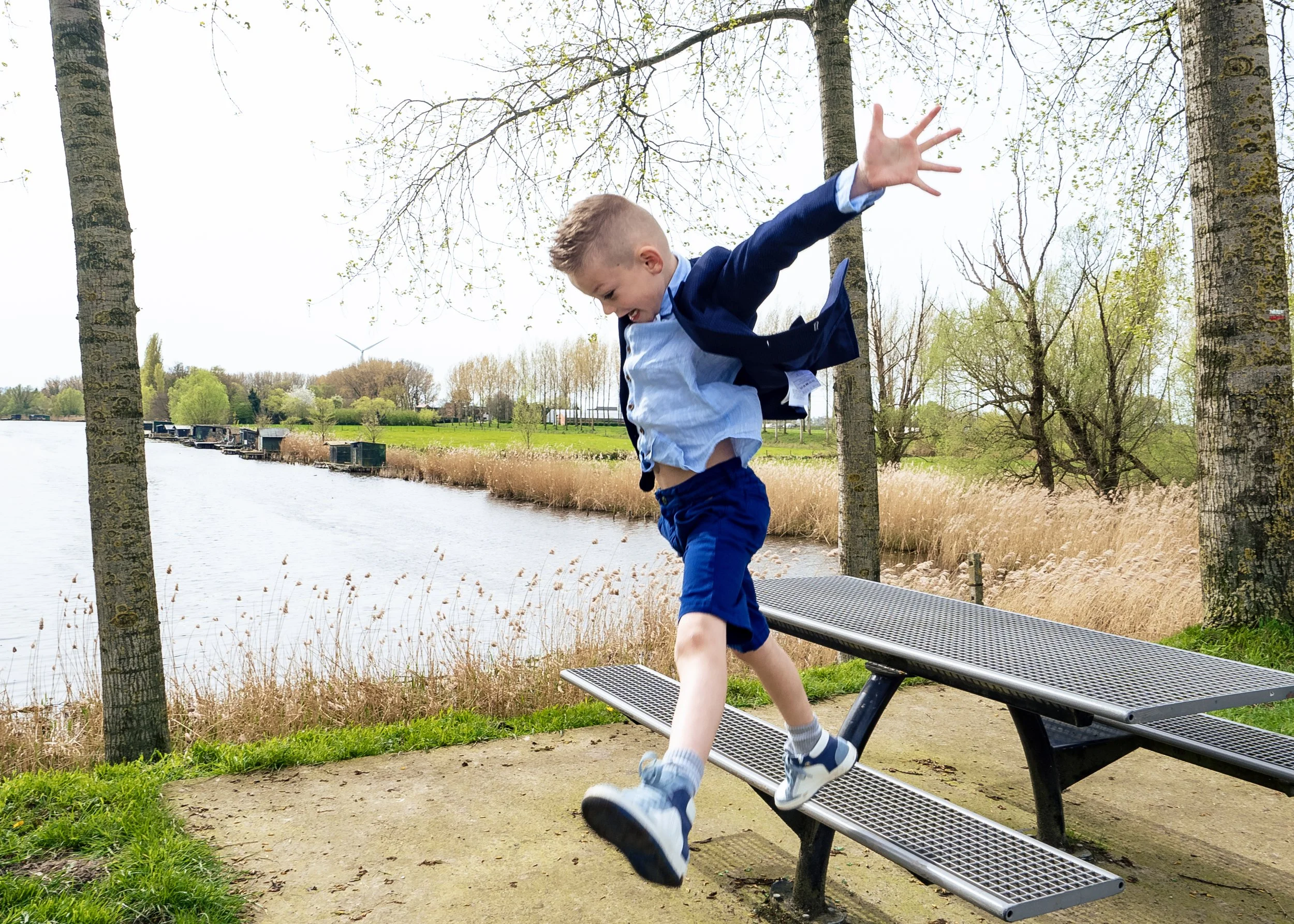 Jongen springt van een parkbankje langs een rivier in een groene omgeving.