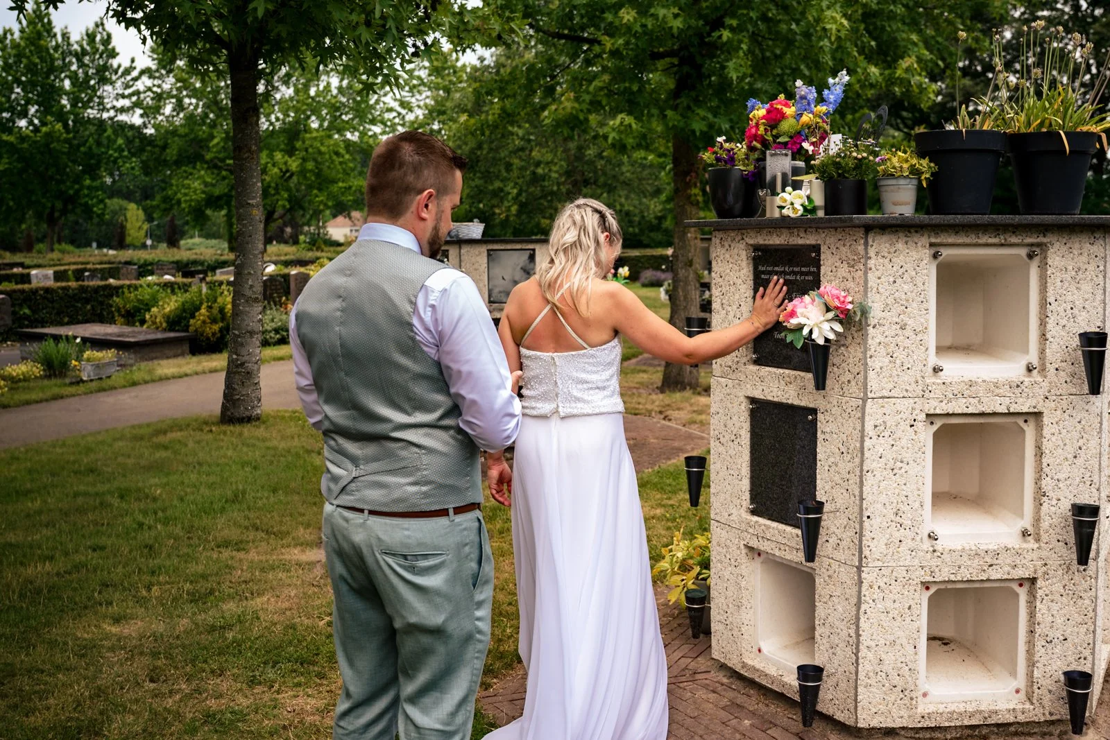 Een paar staat bij een graf in een begraafplaats en legt bloemen neer.