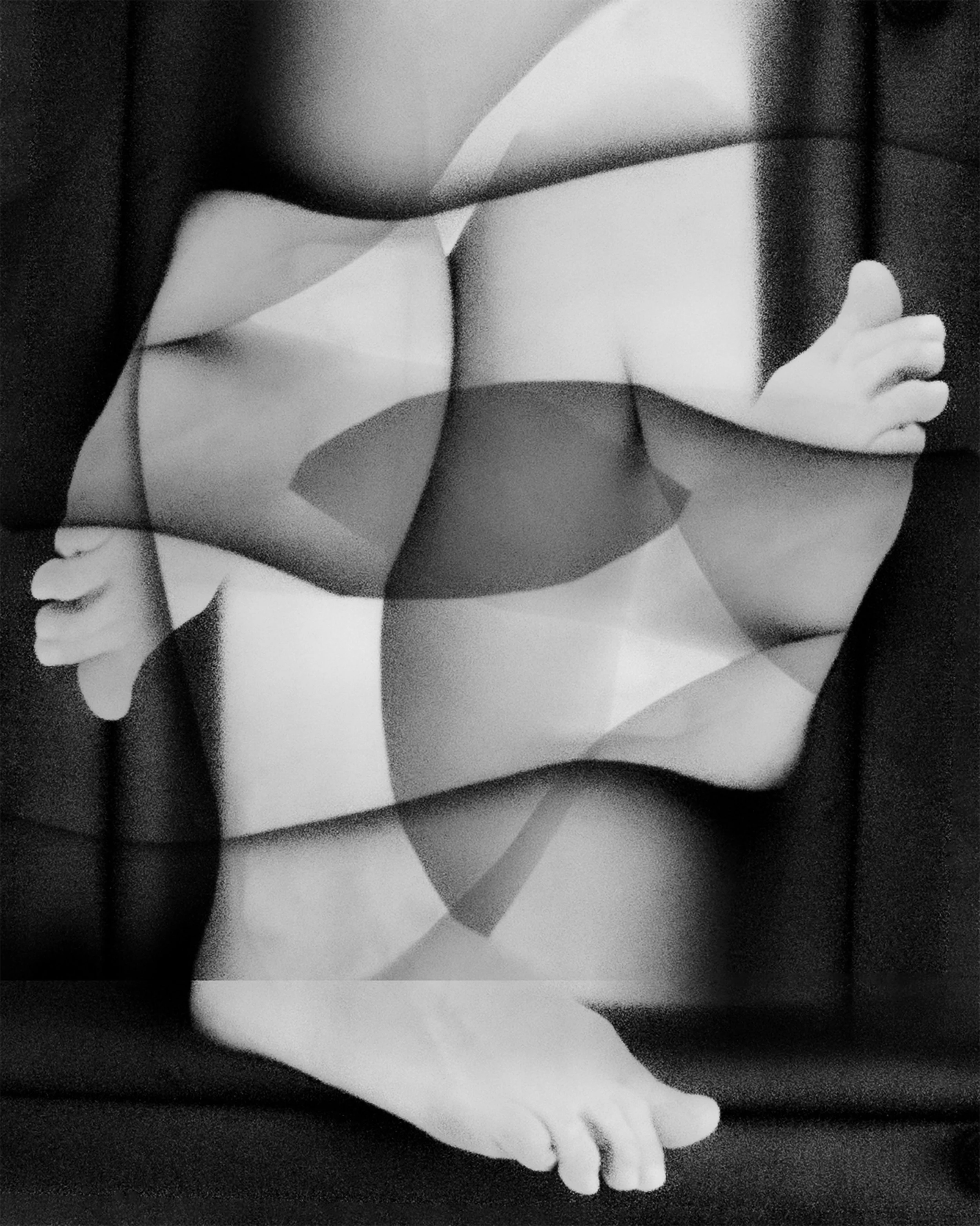 Black and white photo of a person's legs and feet, with one hand resting on the thigh and visible partial view of the torso, in a relaxed pose.