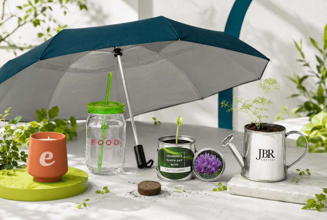 Spring promotional products featuring planter kits, an umbrella, a reusable tumbler and a scented candle in a branded garden setting.