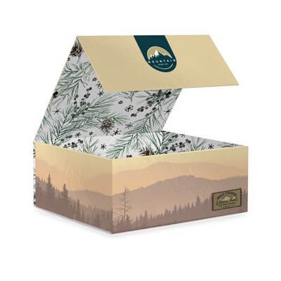 Open magnetic gift box with a cream exterior, botanical printed lid, teal interior logo panel, and kraft crinkle fill.