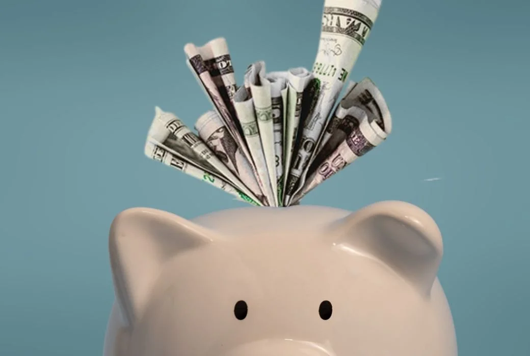 White piggy bank with folded U.S. dollar bills fanned out from the top, symbolizing saving money and budget-friendly marketing.