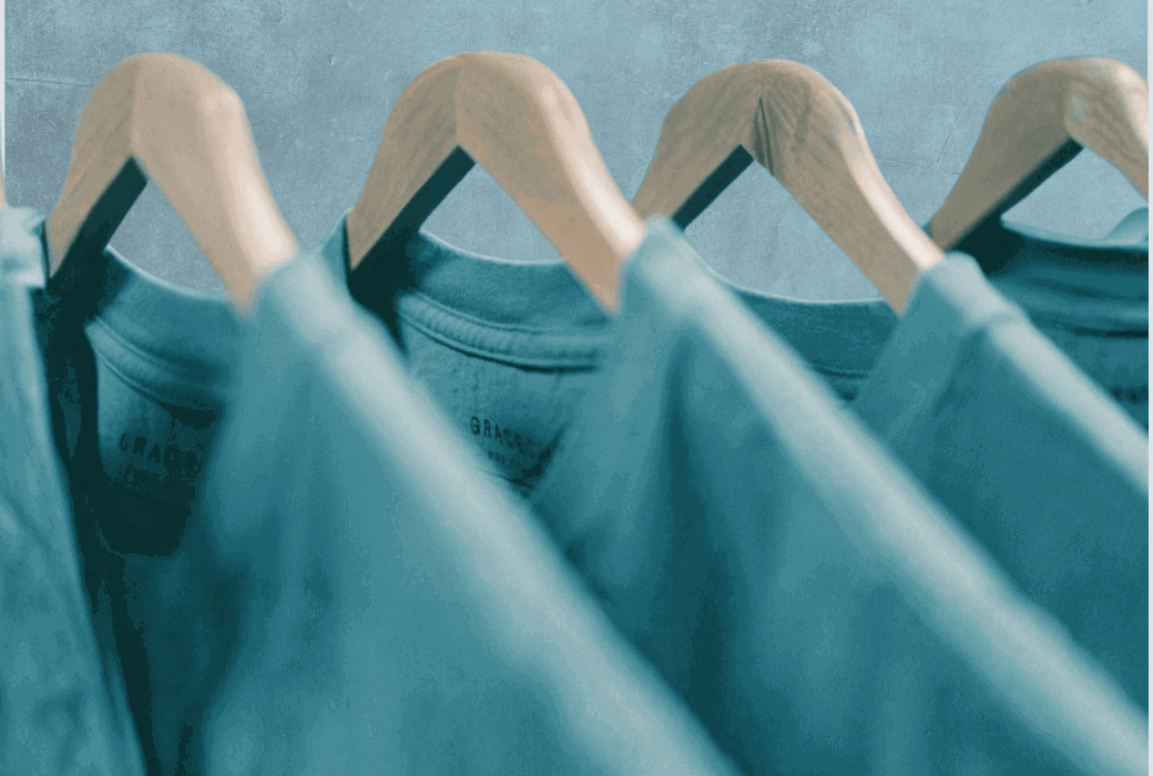 Teal sustainable apparel shirts displayed on wooden hangers.
