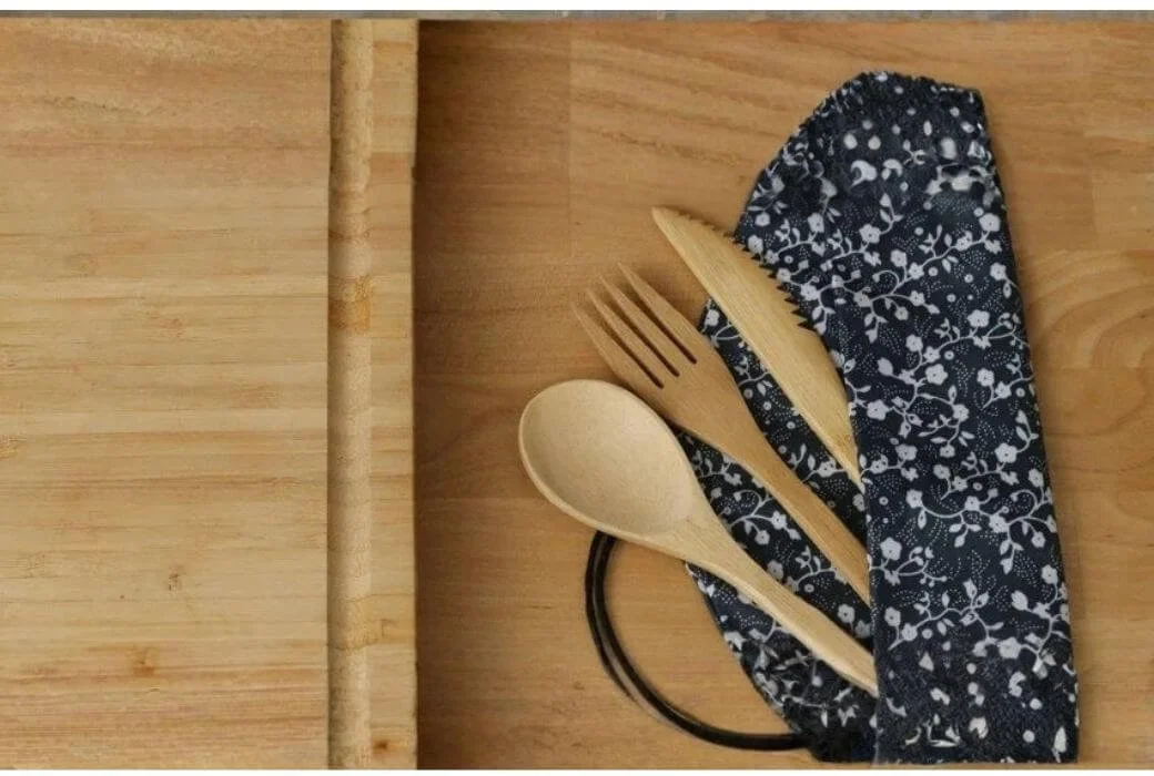 Eco-friendly reusable bamboo utensil set in a fabric pouch, shown on a wooden cutting board for sustainable living.