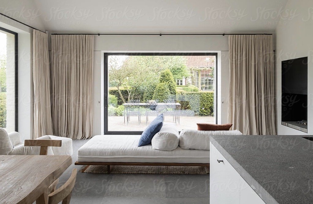 Living room with large glass sliding doors opening to a backyard patio with outdoor furniture and greenery.