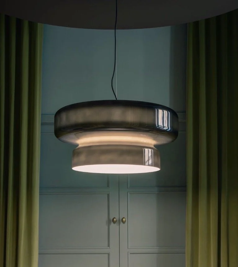 Close-up of a modern metallic ceiling light fixture hanging from a black cord in a room with green curtains and blue walls. Dining room project in Kilchberg, along the lake of Zurich. 