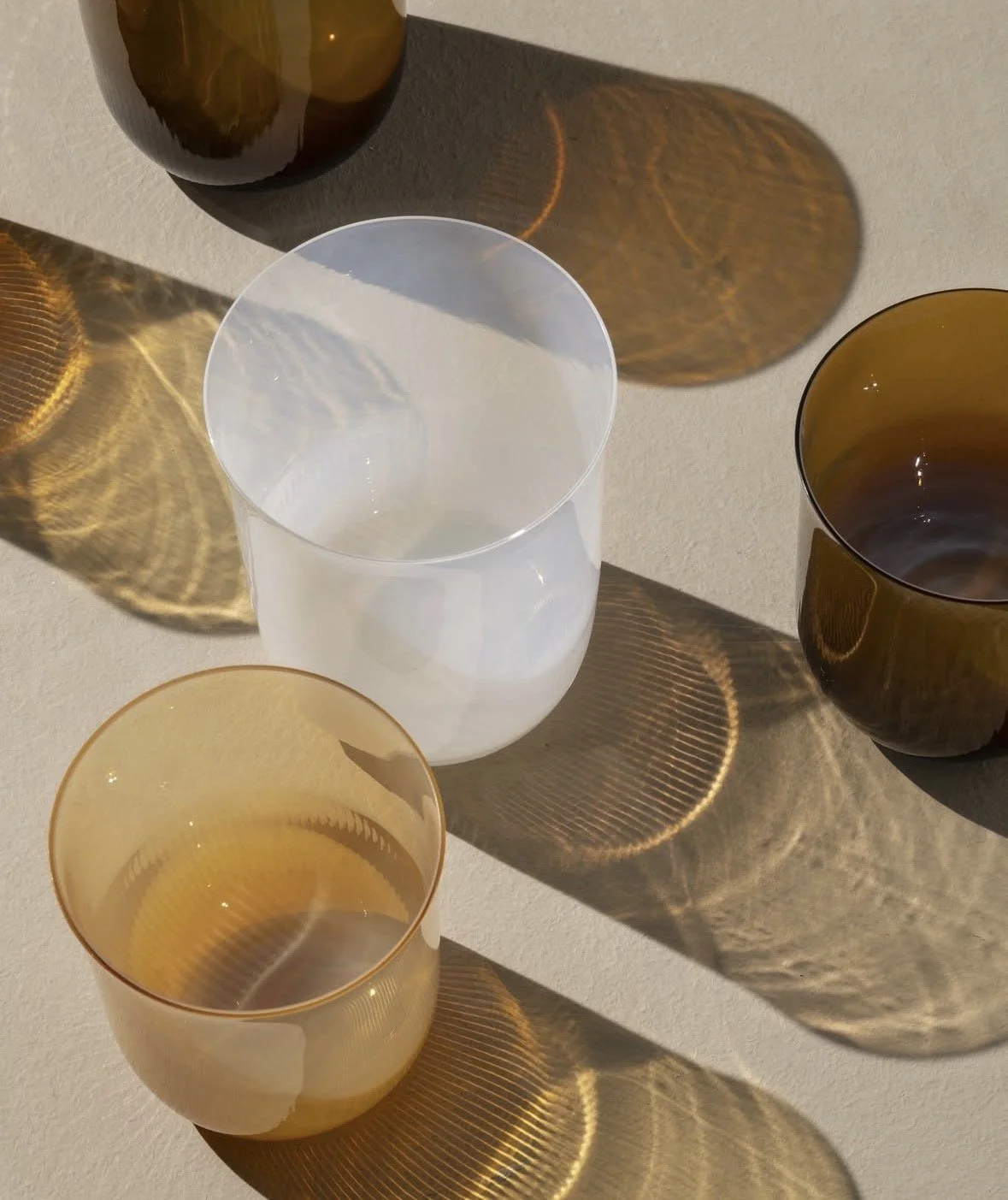 Amber and frosted glass tumblers casting warm shadows in natural sunlight. Discover tableware and home accessories with Maison Barbara, an interior design studio serving Zurich and Lake Zurich.