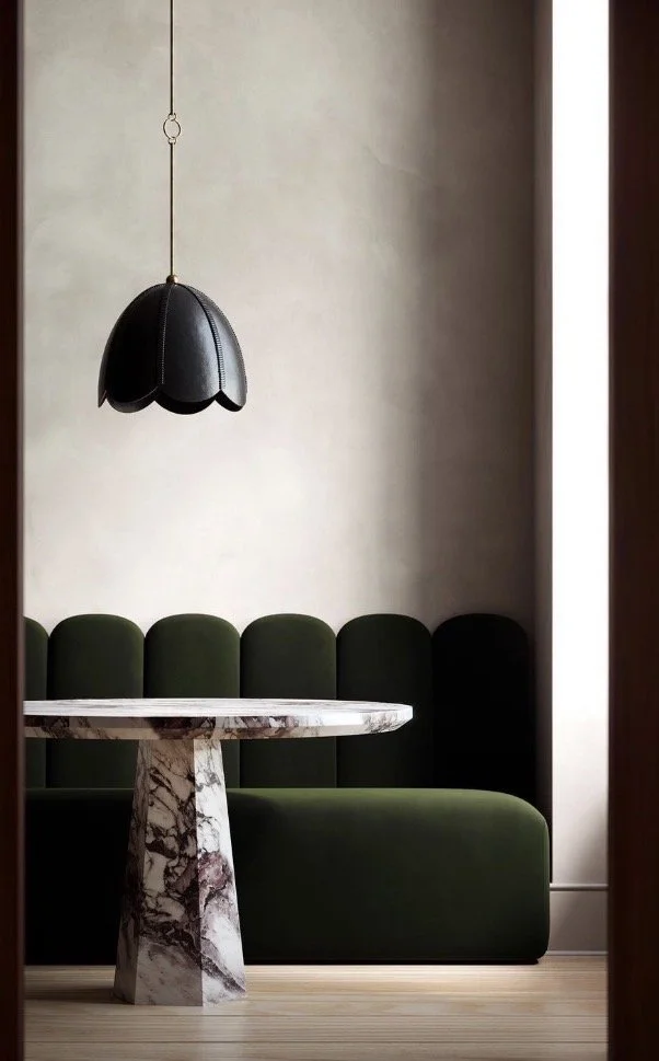 A room corner with a green upholstered bench, a white marble round table, and a black pendant lamp hanging from the ceiling.