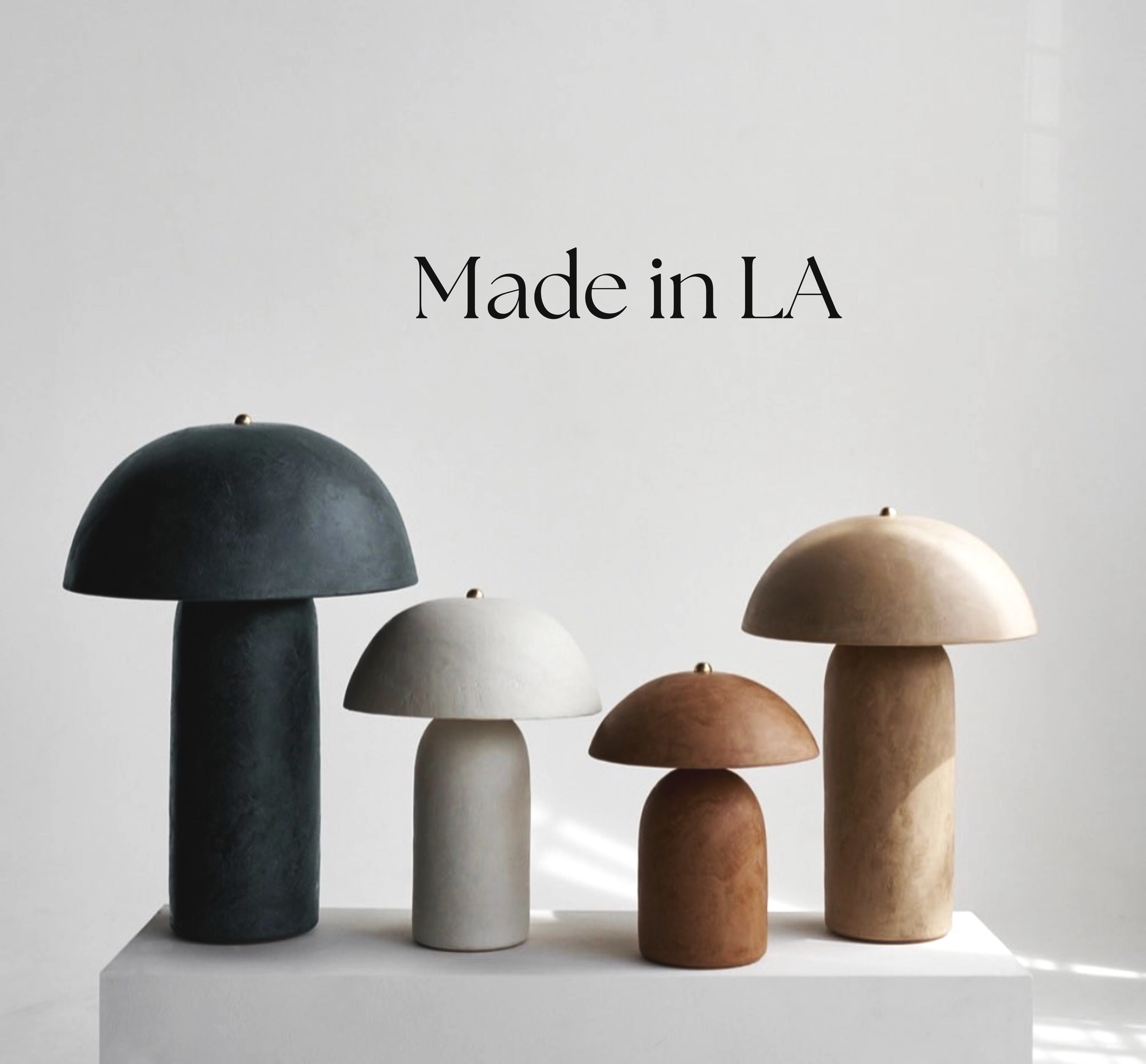 Set of seven wooden and ceramic mushroom-shaped objects in black, white, beige, and brown, arranged on a white surface with a plain white wall background. Available in Oberrieden at Maison Barbara Studio.