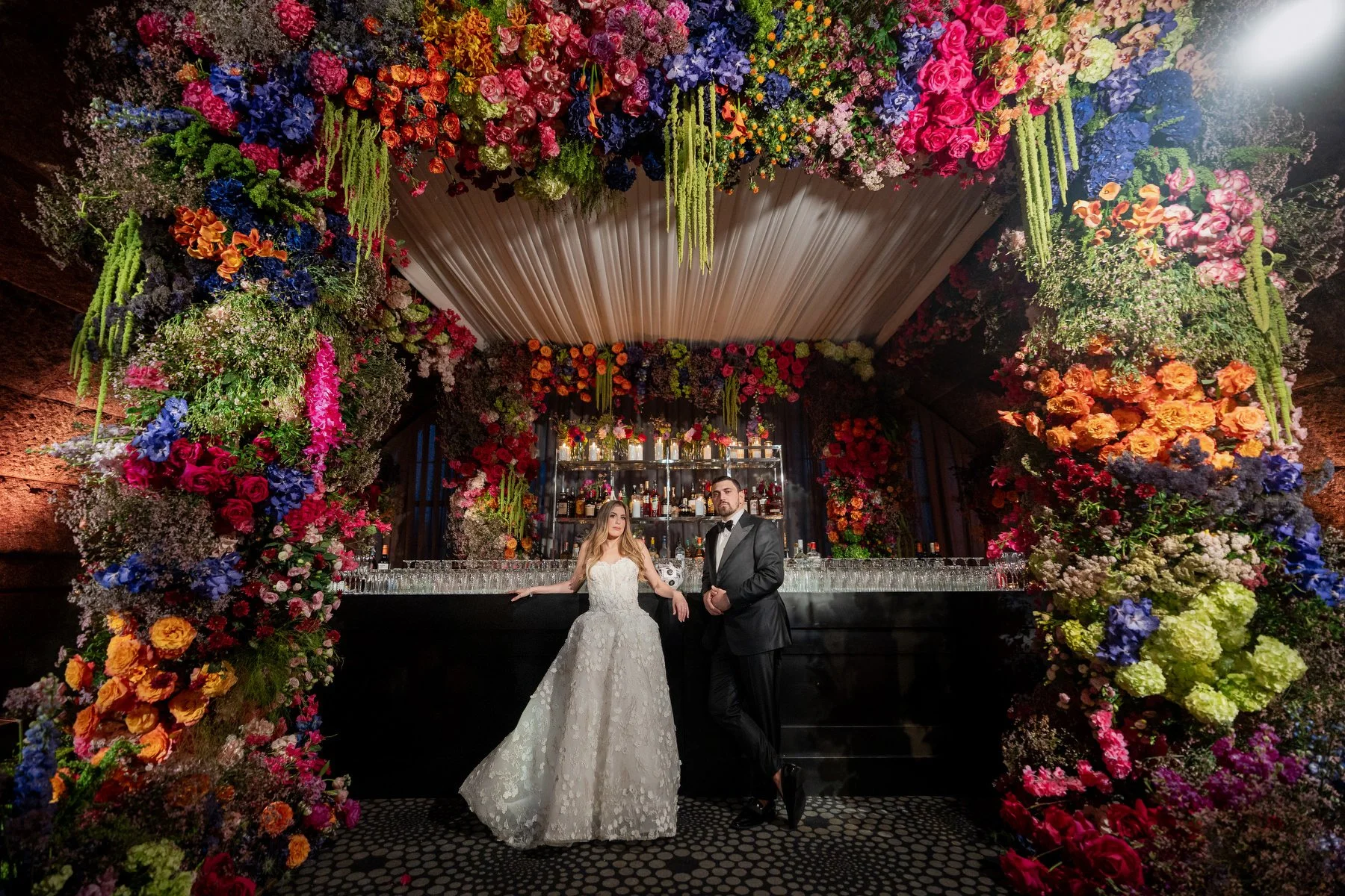 Couple at bar with vibrant floral backdrop at Guastavinos wedding