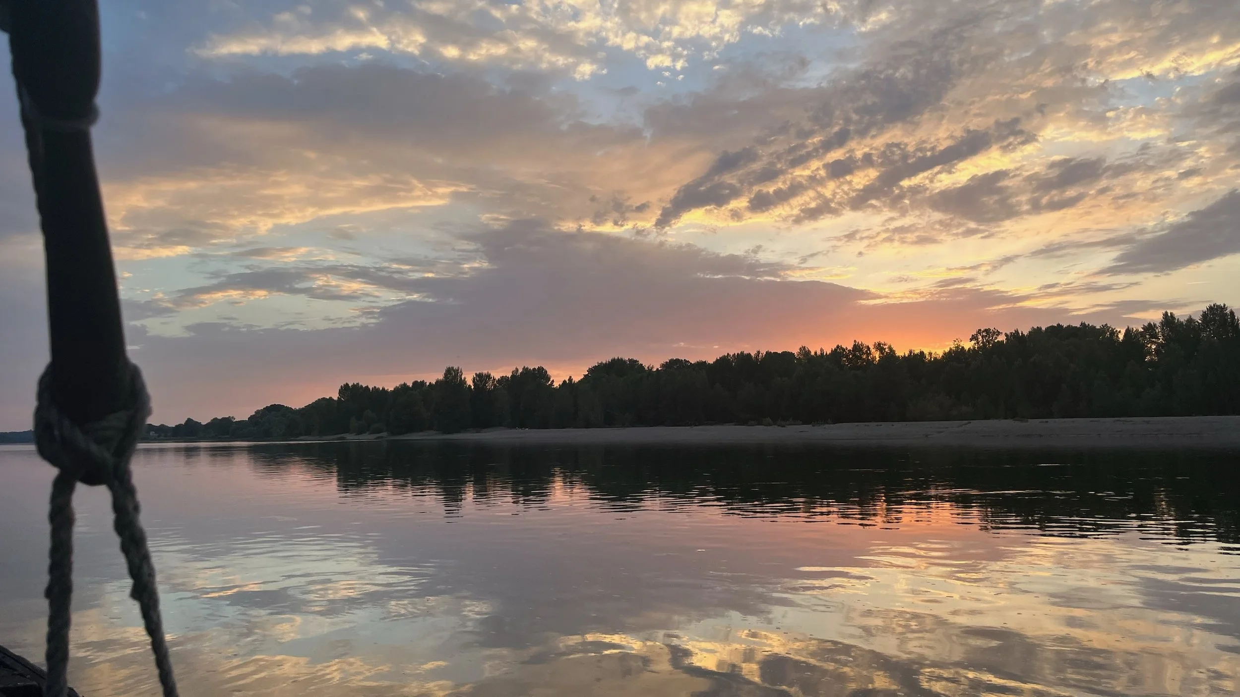 Coucher de soleil sur une rivière bordée d'arbres, vu depuis un bateau, avec une corde en premier plan