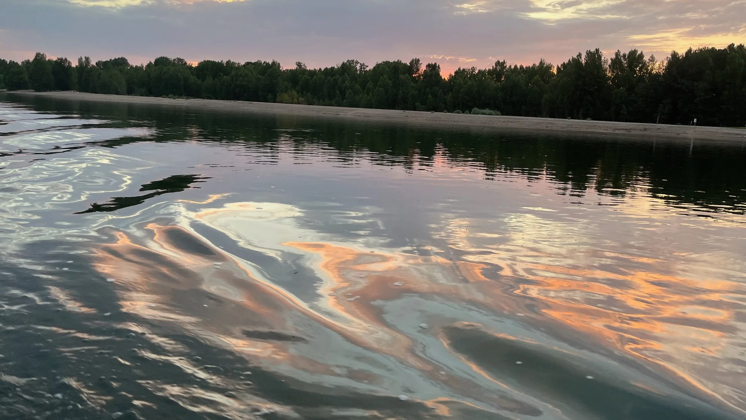 Coucher de soleil se reflétant sur une rivière calme entourée d'arbres.