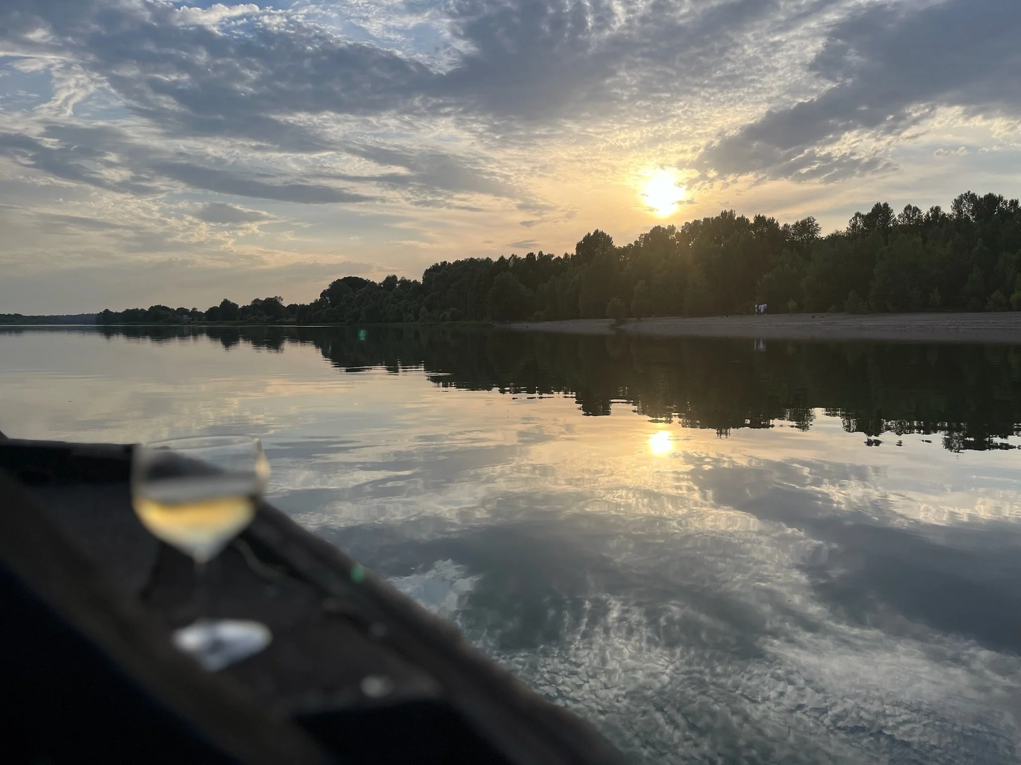 Coucher de soleil sur un lac avec des arbres en arrière-plan et de légères nuages dans le ciel.