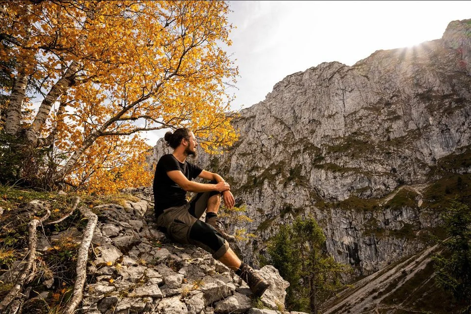 Naturfotograf, Bergwanderführer und Krankenpfleger Sebastian Frölich unter einer herbstlich gefärbten Birke auf einem Felsvorsprung in den bayrischen Voralpen.