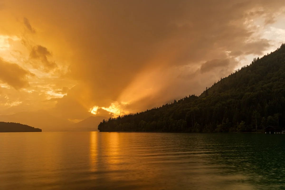 Regen und Gewitterlicht während Sonnenuntergang am Ufer des Walchensee in den bayrischen Alpen.