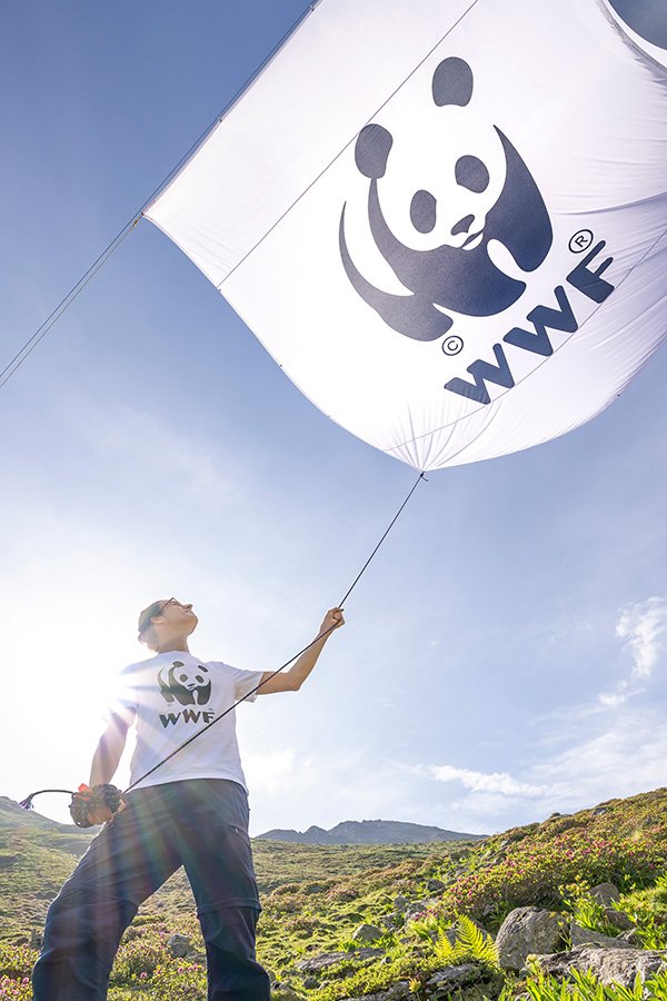 Maximilian Frey vom WWF hält das WWF Banner im bedrohten Platzertal im Gegenlicht der Sonne.