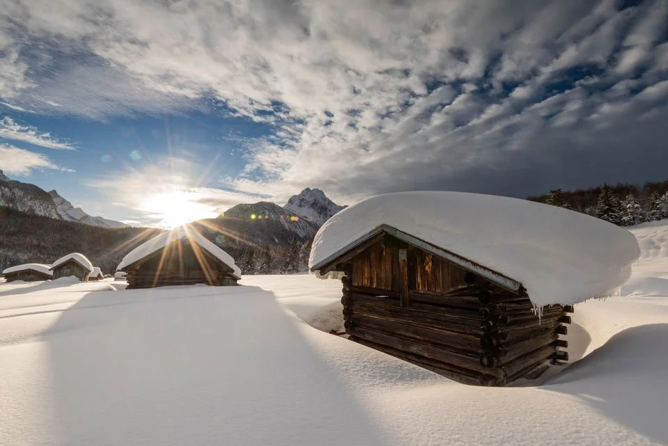 Heuschober oberhalb von Mittenwald im Tiefschnee, im Hintergrund das Wettersteingebirge, Wolken und der Sonnenuntergang mit schönem Sonnenstern