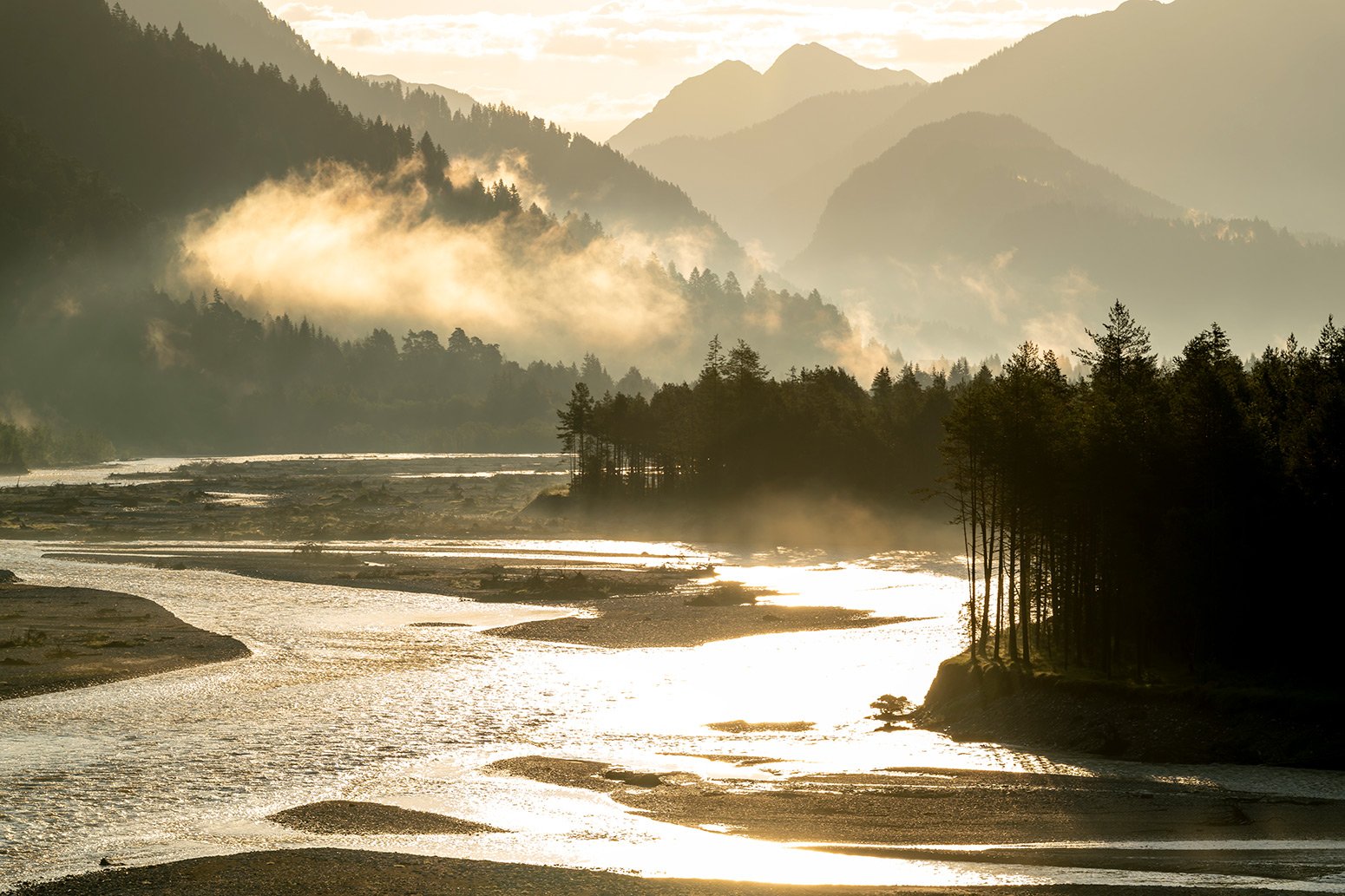 Der Tiroler Lech bei Elmen im Gegenlicht der aufgehenden Sonne mit tiefen Wolken und Nebel. Das verzweigte Flusssystem birgt einige Schätze der Natur.