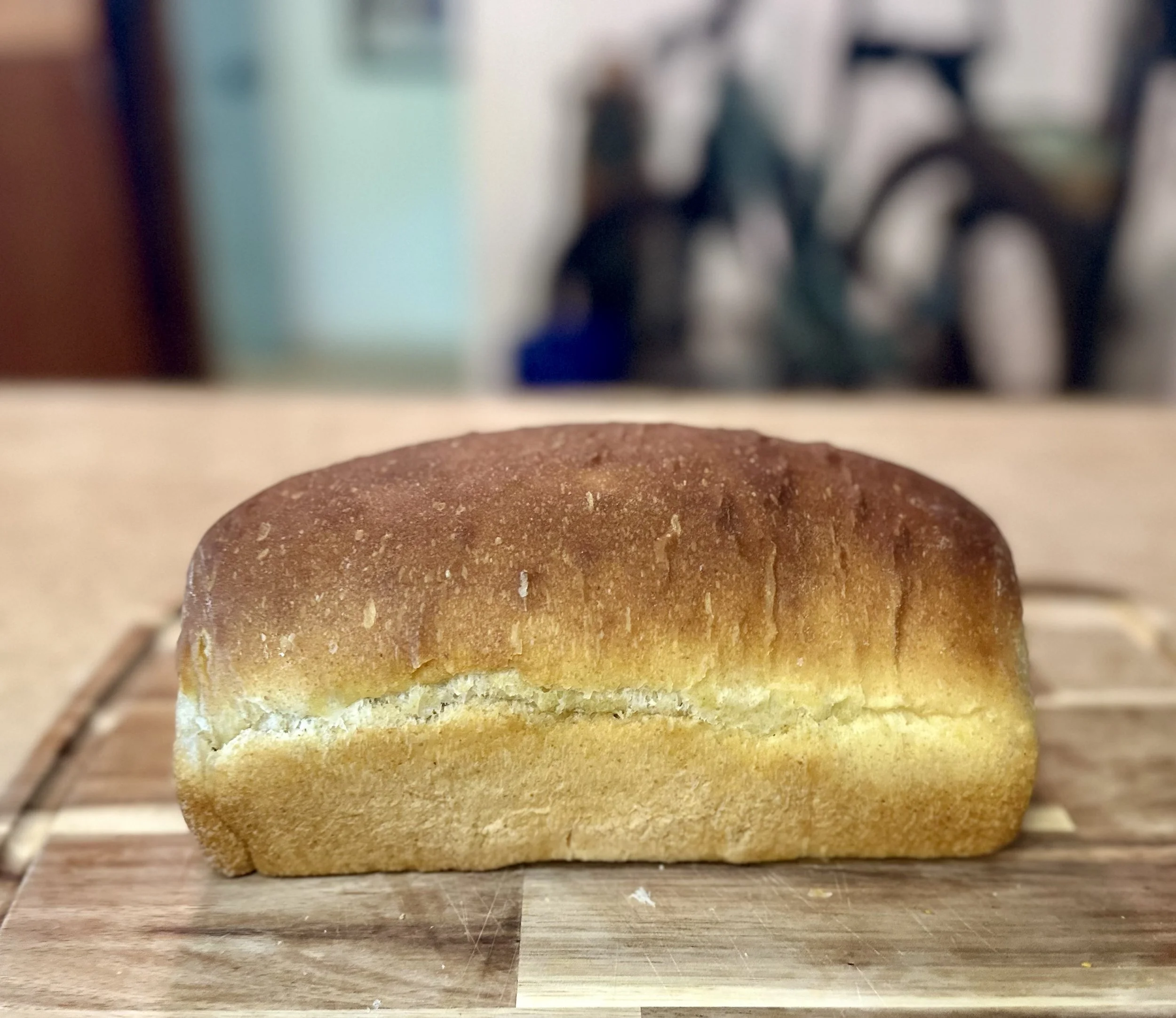 Homemade sourdough sandwich bread loaf with golden crust, baked in a pan and resting on a wooden cutting board