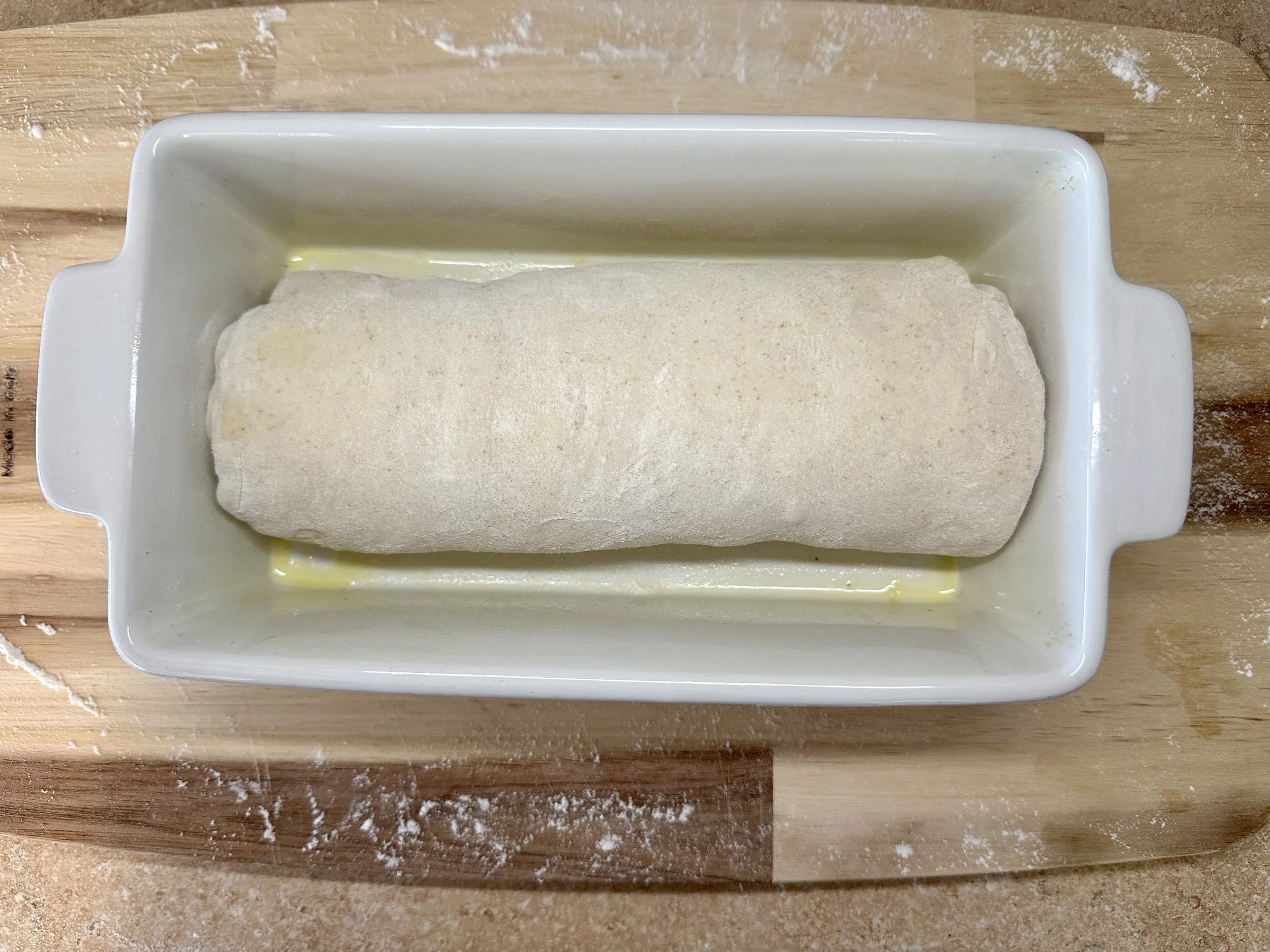 Rolled sourdough dough placed seam-side down in an oiled white loaf pan, ready for final proof
