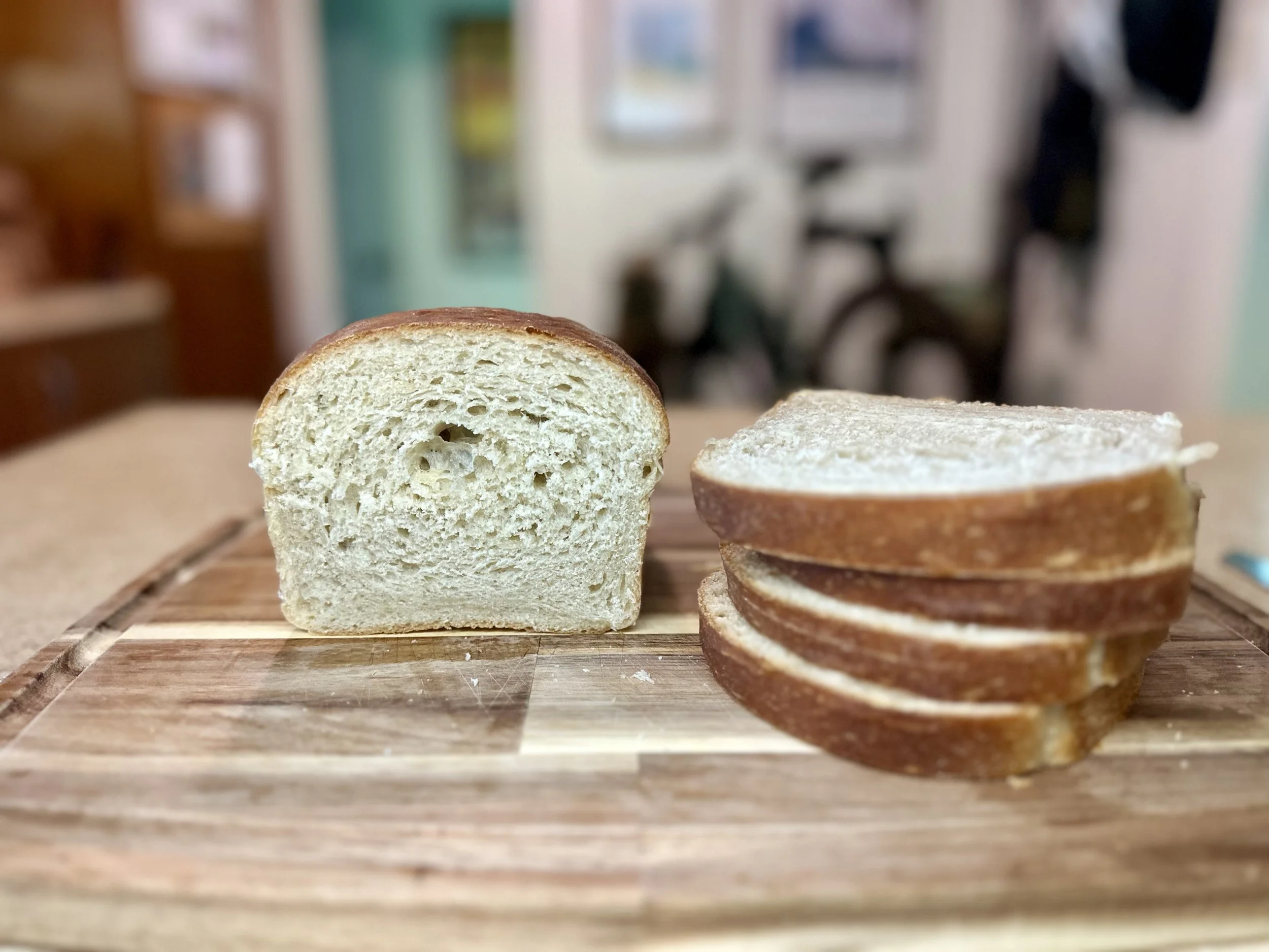 Sourdough sandwich bread loaf with a soft interior crumb and several slices on a wooden cutting board