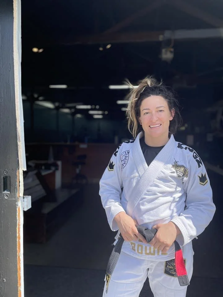 Person smiling on a beach with wind in hair, ocean and sand visible in background.