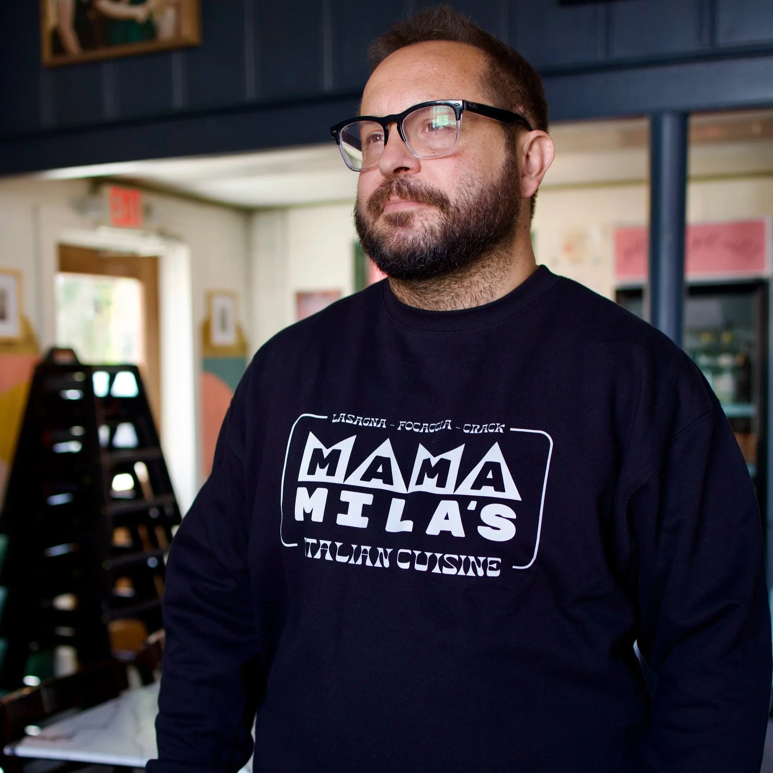 Mateo wearing the Black sweatshirt with a white vintage Mama Mila's design on it, featuring the words Focaccia, Lasagna, Crack and Italian Cuisine"