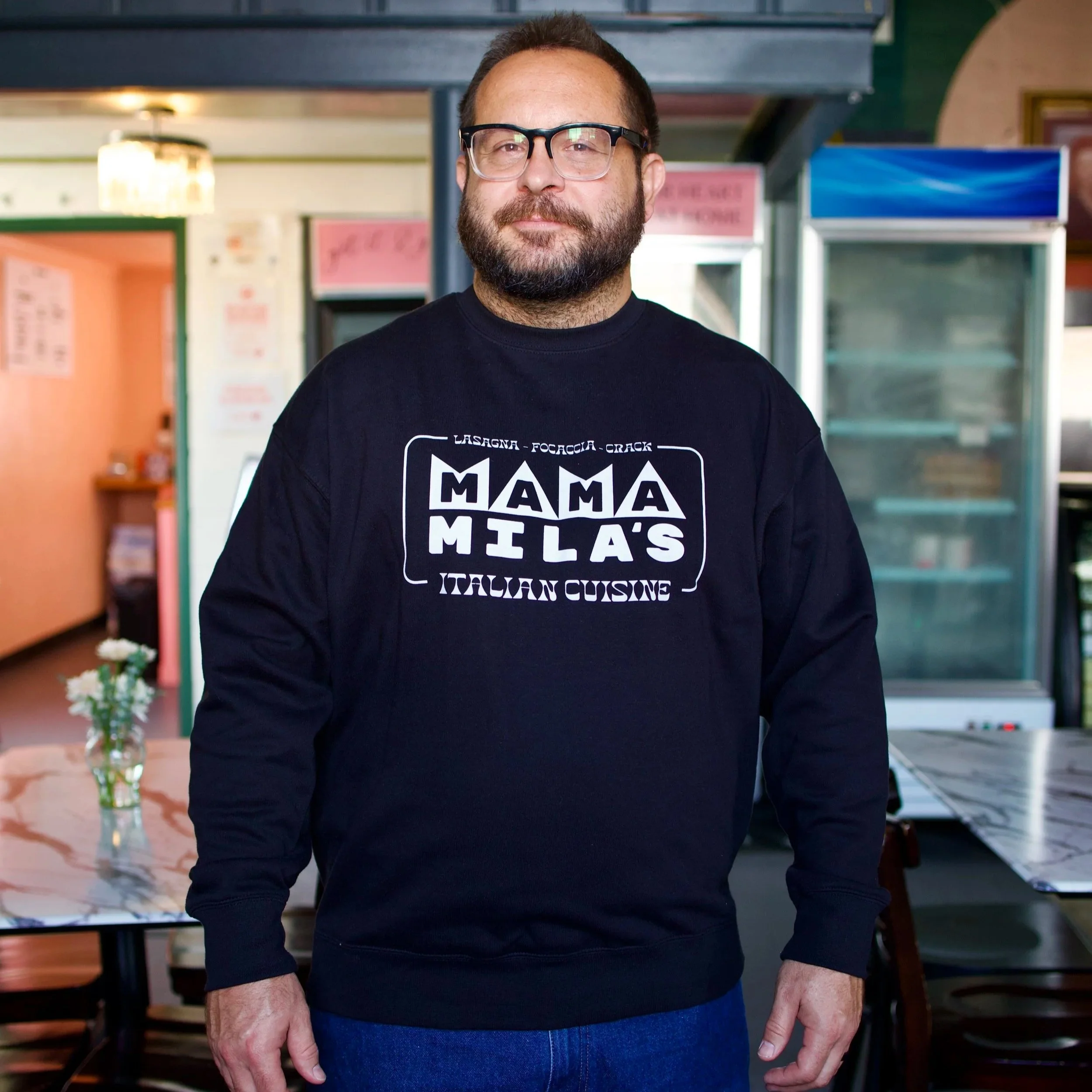Mateo wearing the Black sweatshirt with a white vintage Mama Mila's design on it, featuring the words Focaccia, Lasagna, Crack and Italian Cuisine"